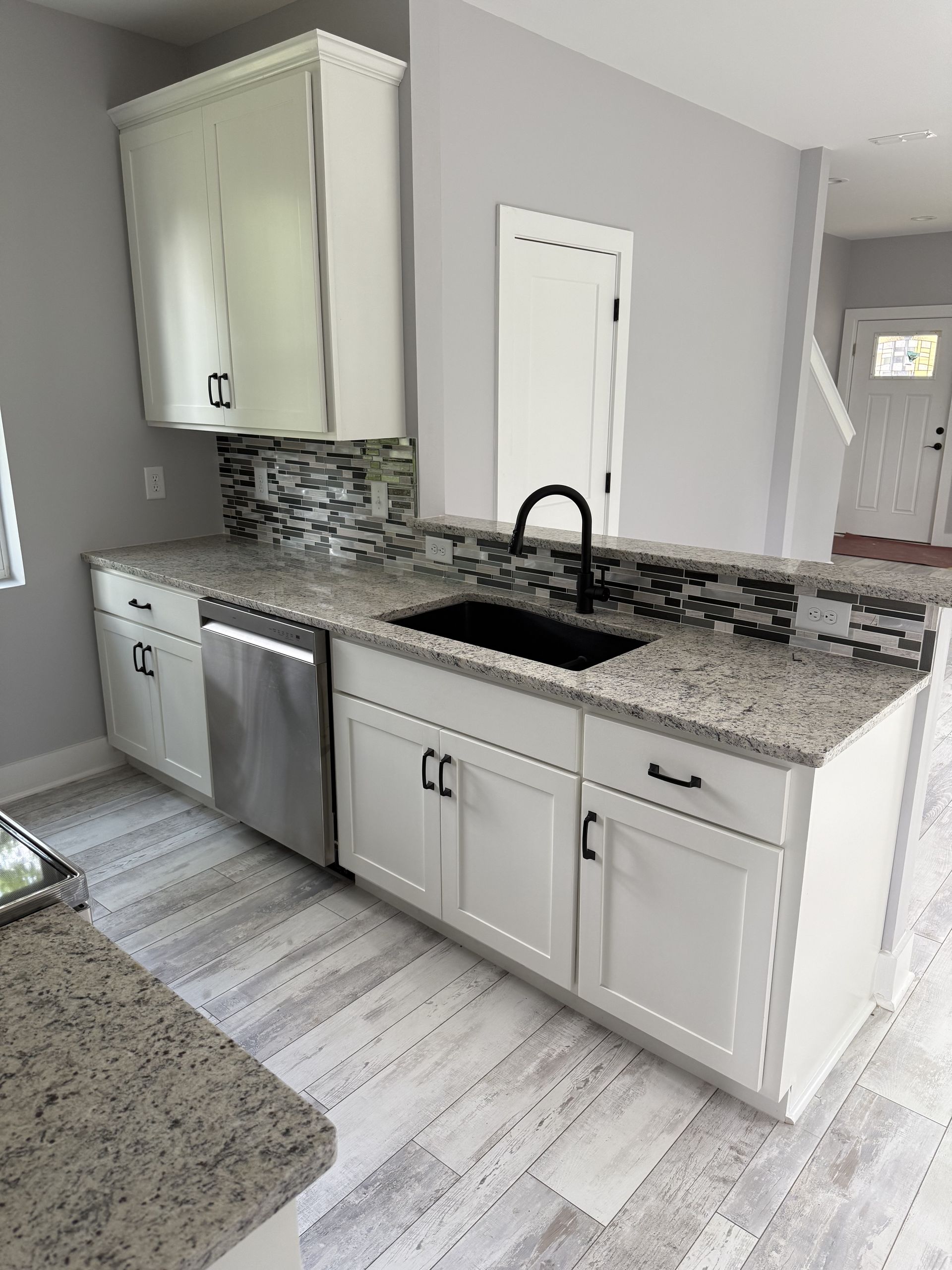 Bright kitchen with white cabinets, gray granite counters, mosaic backsplash, and black sink faucet