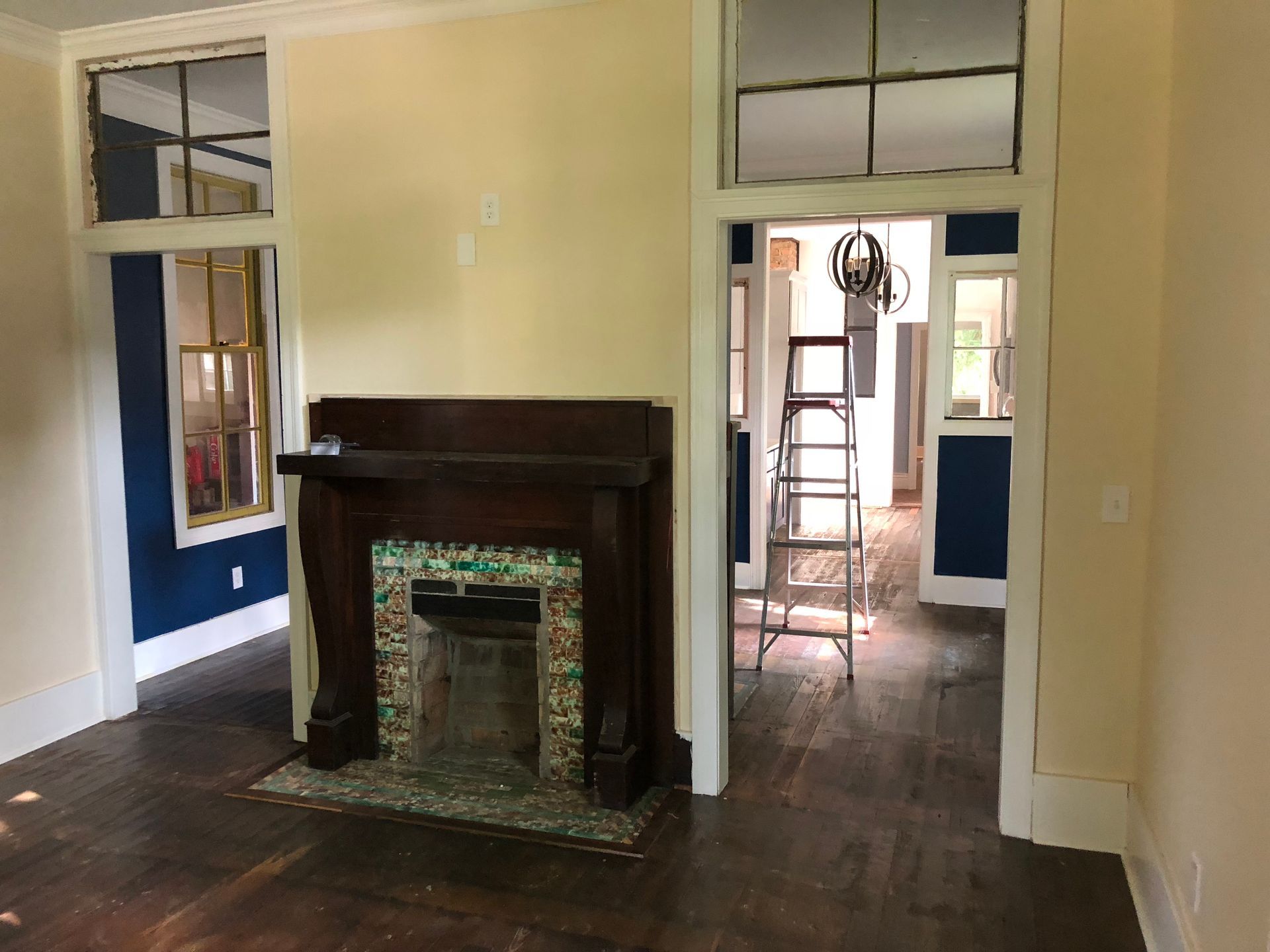 Empty room with dark wood fireplace, yellow walls, and doorway opening to a ladder in the back room