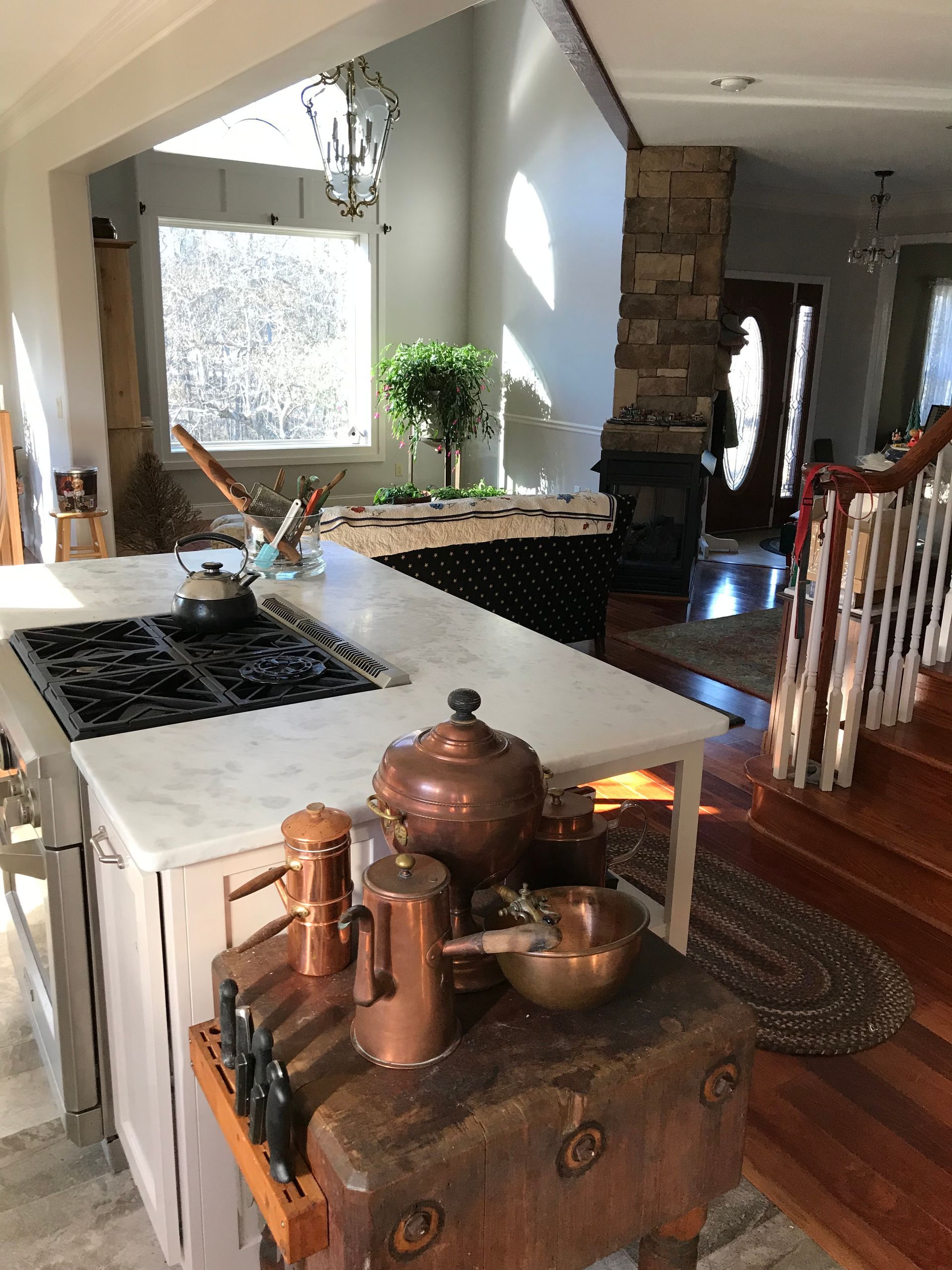 Stylish kitchen with white island, black stovetop, copper decor, and staircase in the background