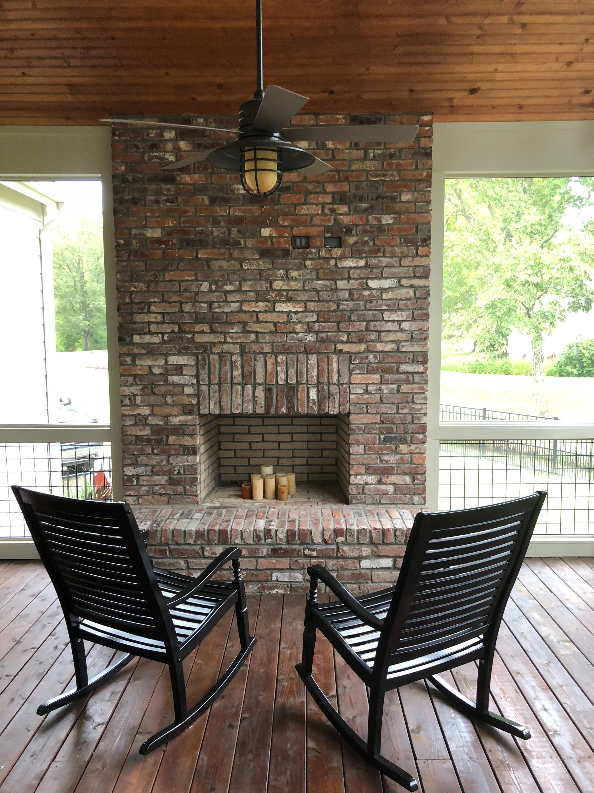 Covered patio with brick fireplace, two black rocking chairs, and a ceiling fan.