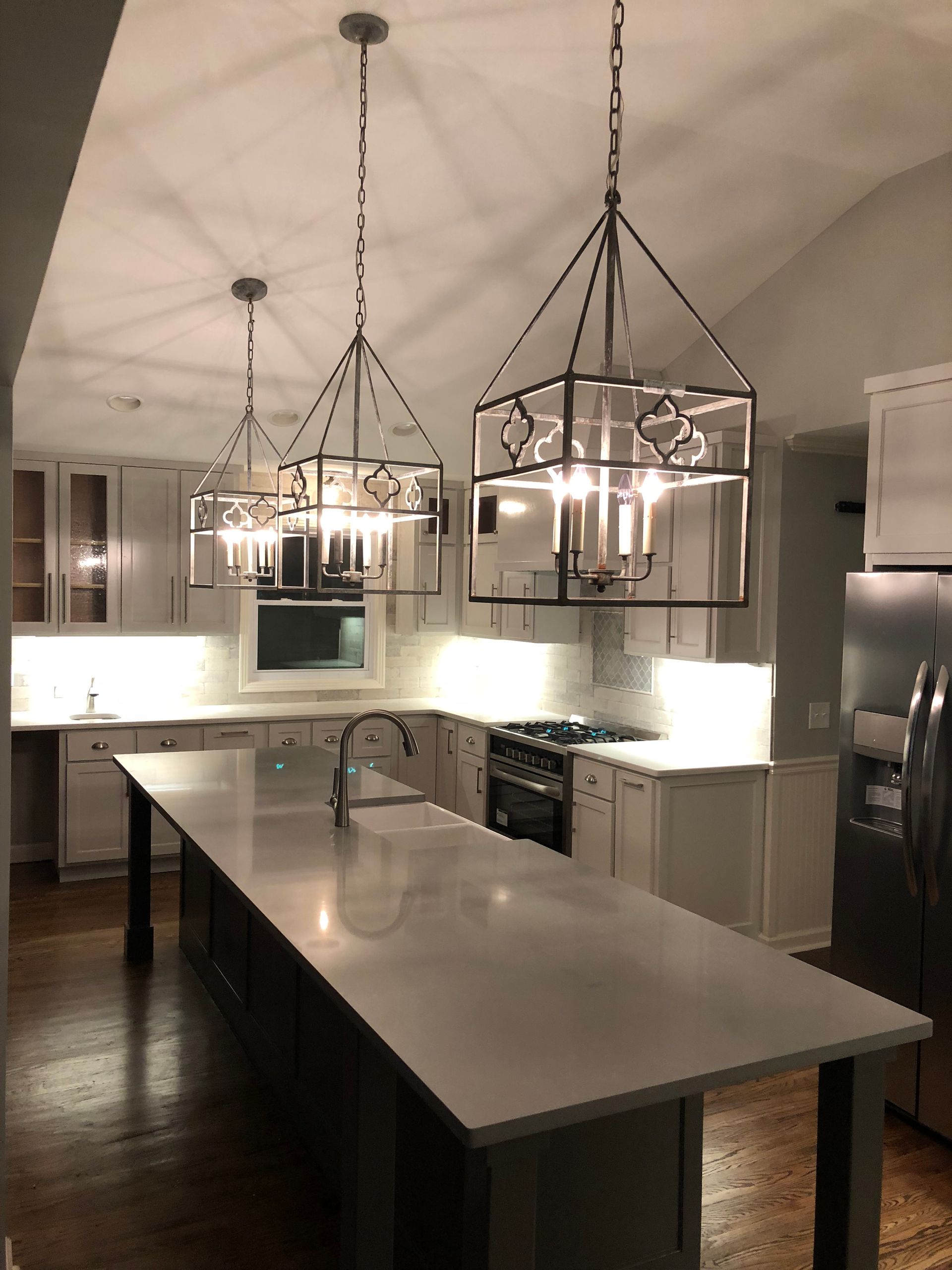 Modern kitchen with large island, pendant lights, stainless appliances, and white cabinetry.