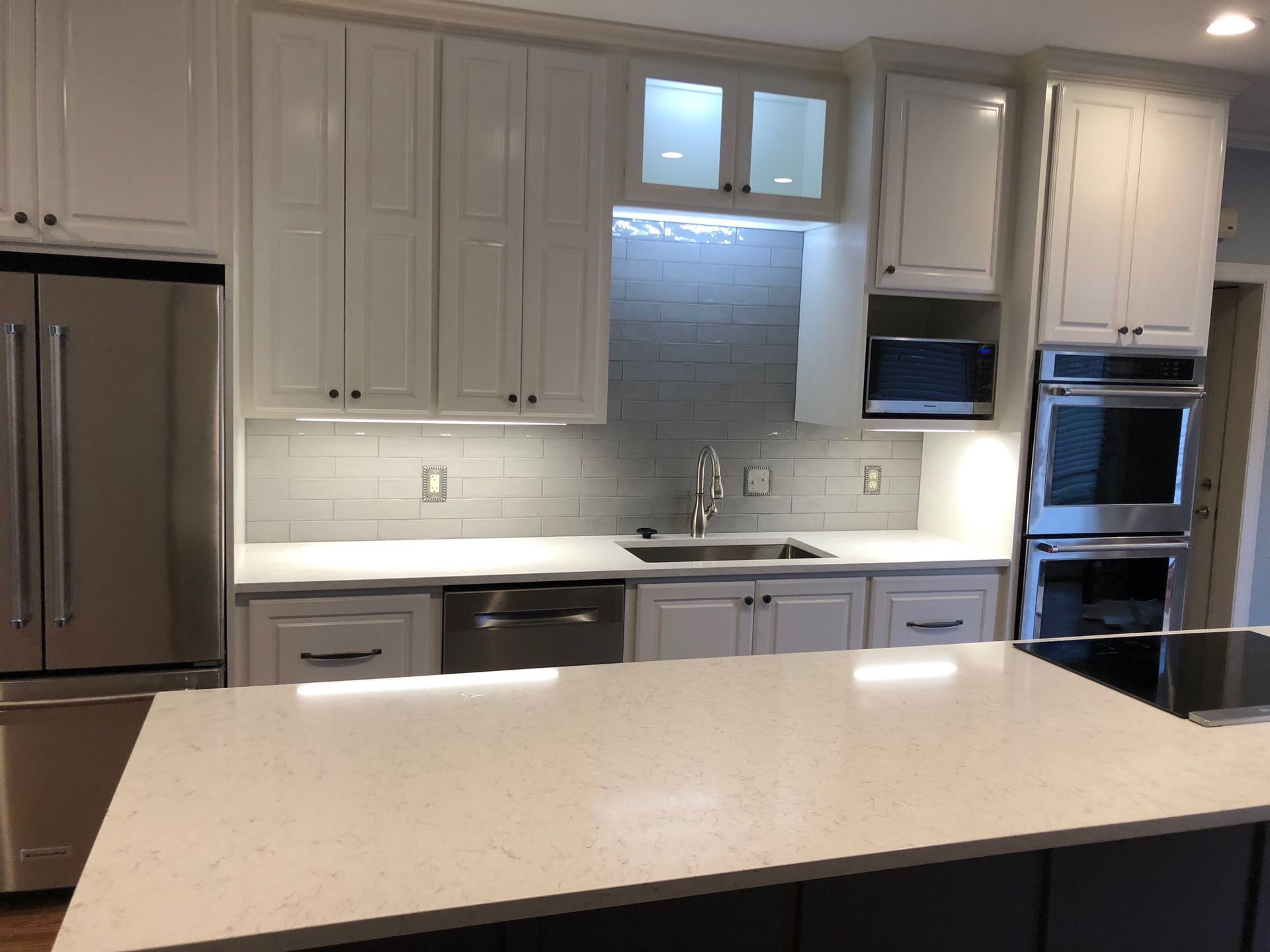 Modern kitchen with white cabinets, stainless steel appliances, and a large light-colored island counter.