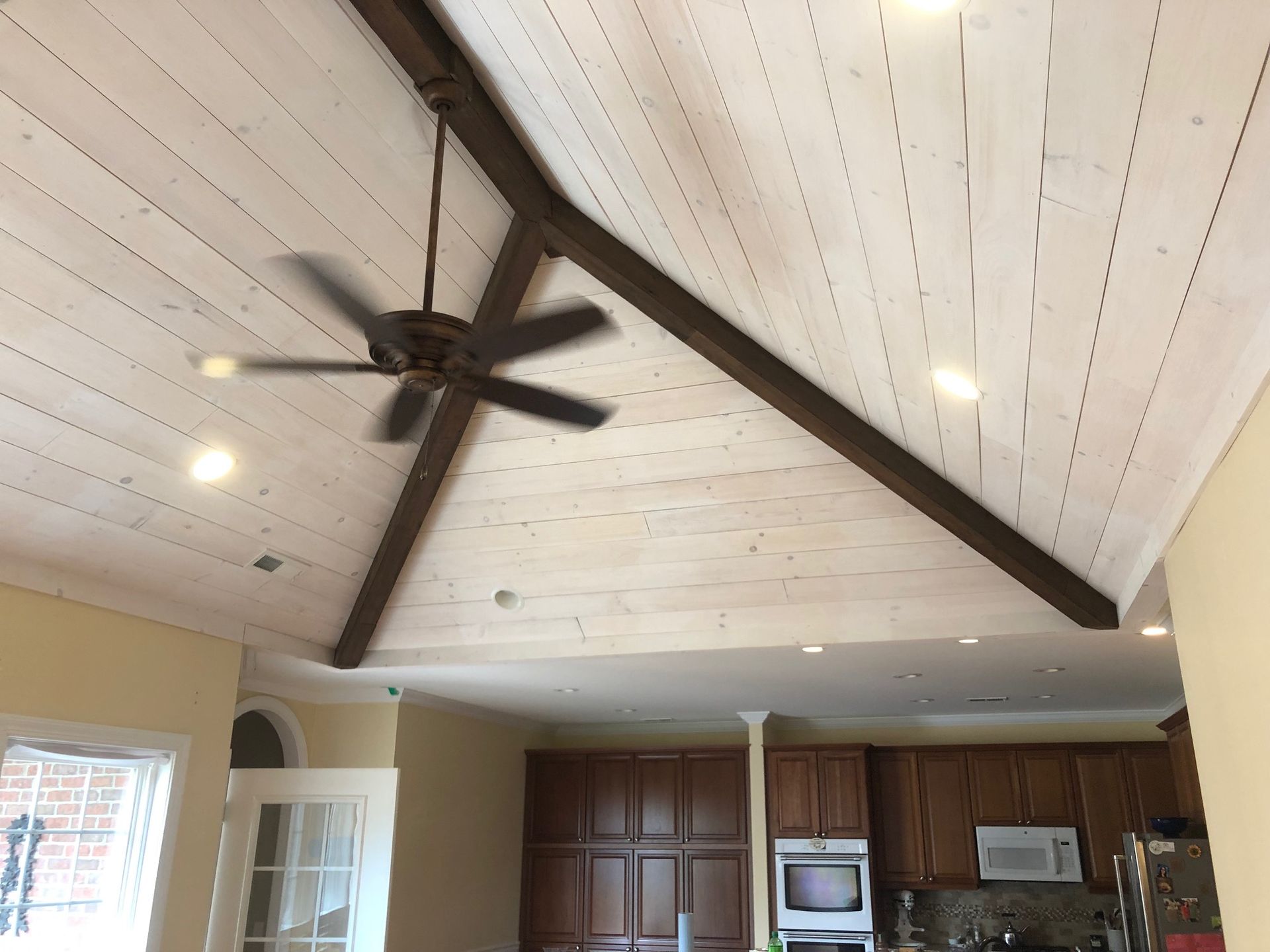 Vaulted ceiling with dark wood beams, ceiling fan, recessed lights, and kitchen cabinets below