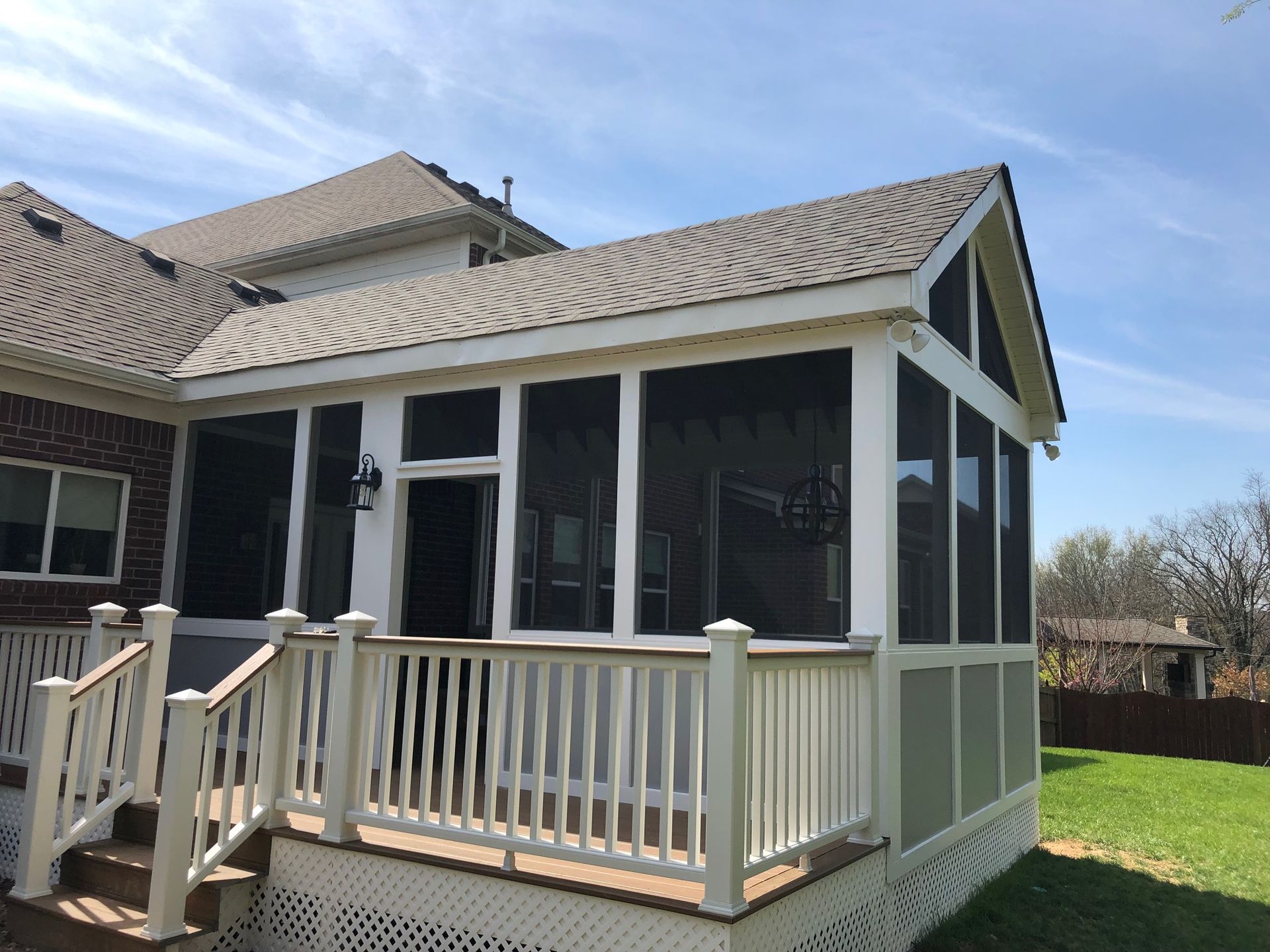 Screened porch with beige railings and gray roof attached to a house on a grassy yard.