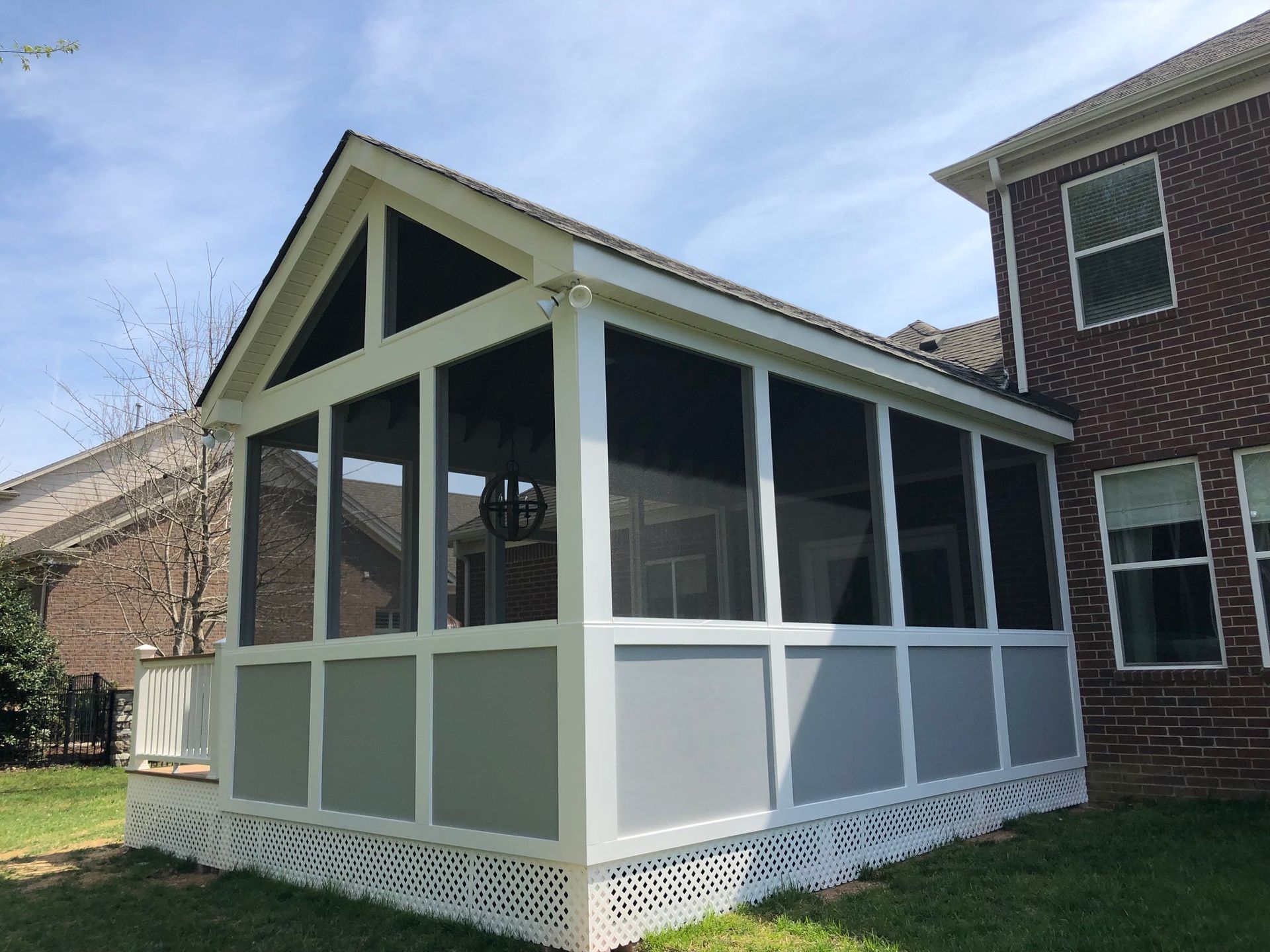 Screened porch with white trim and green roof attached to a brick house