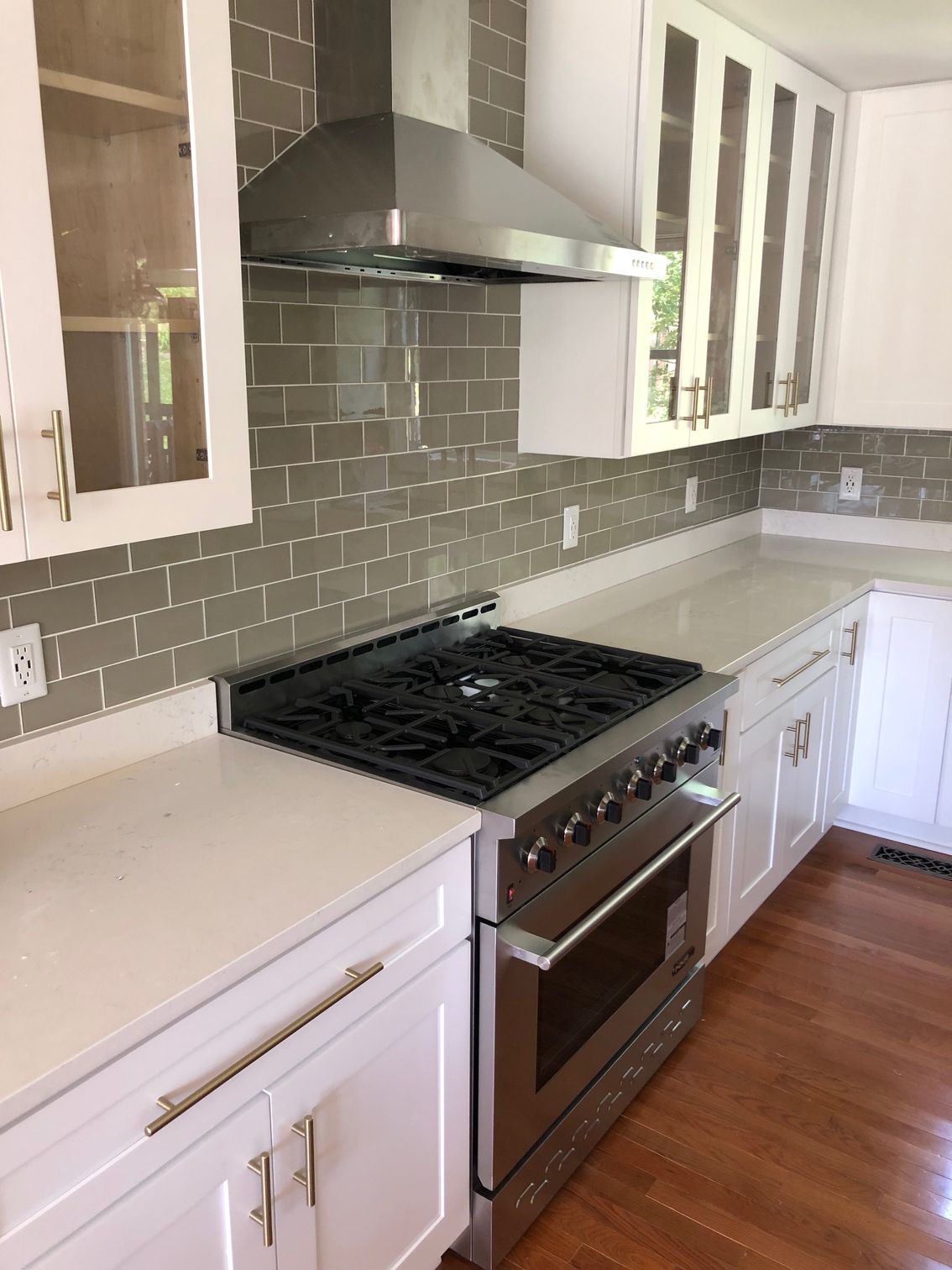 Modern kitchen with stainless steel range and hood, gray tile backsplash, white cabinets, and wood floor