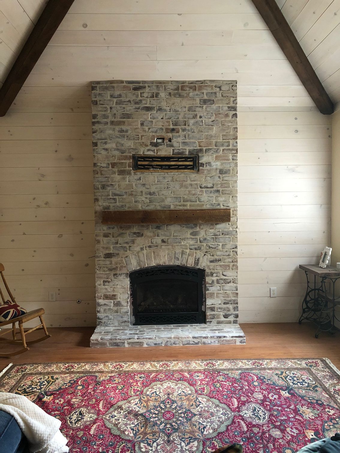 Brick fireplace centered in a rustic room with wood-paneled walls and a red patterned rug