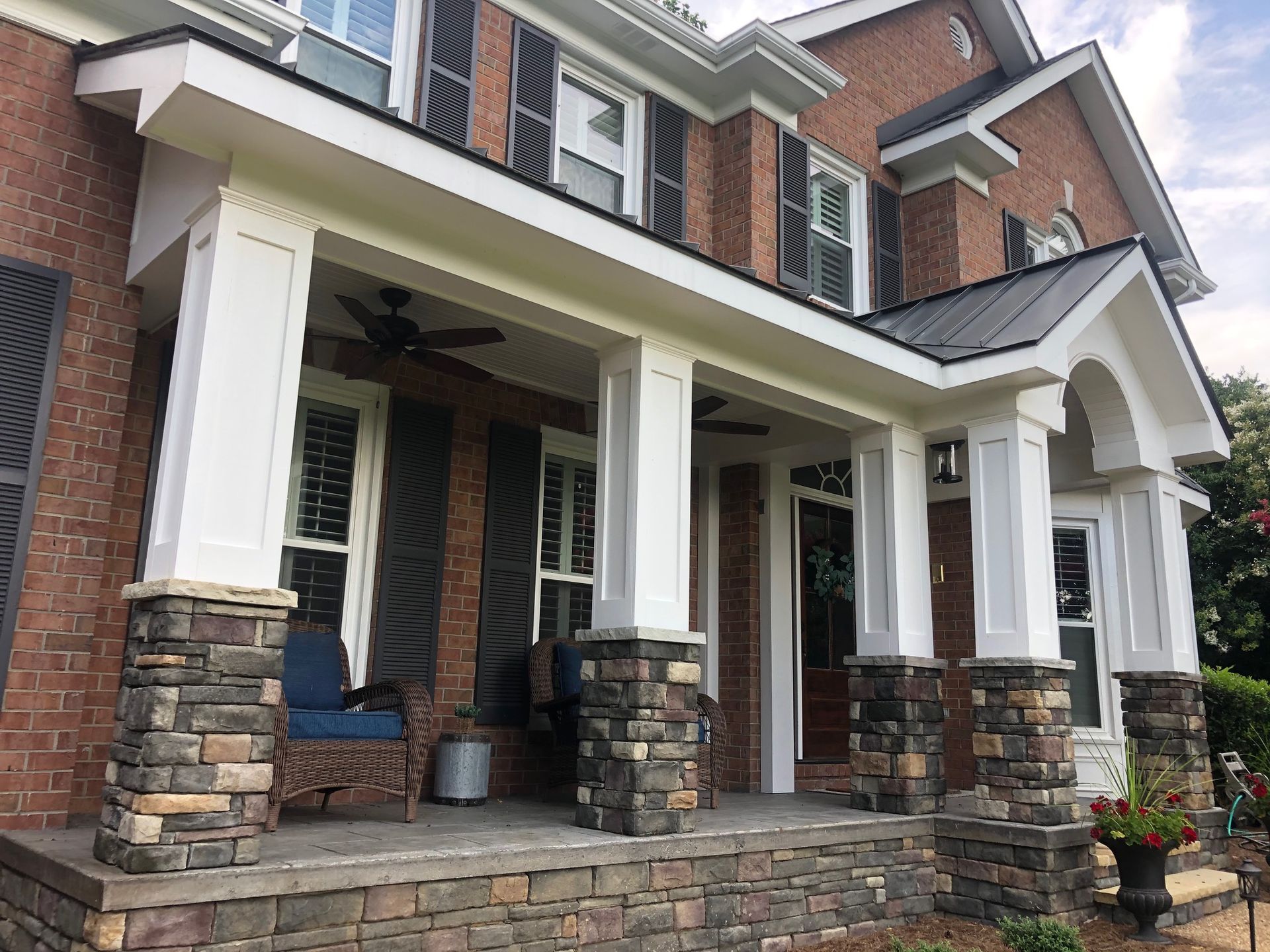 Brick house front porch with white columns, stone bases, and a blue chair on the left side.