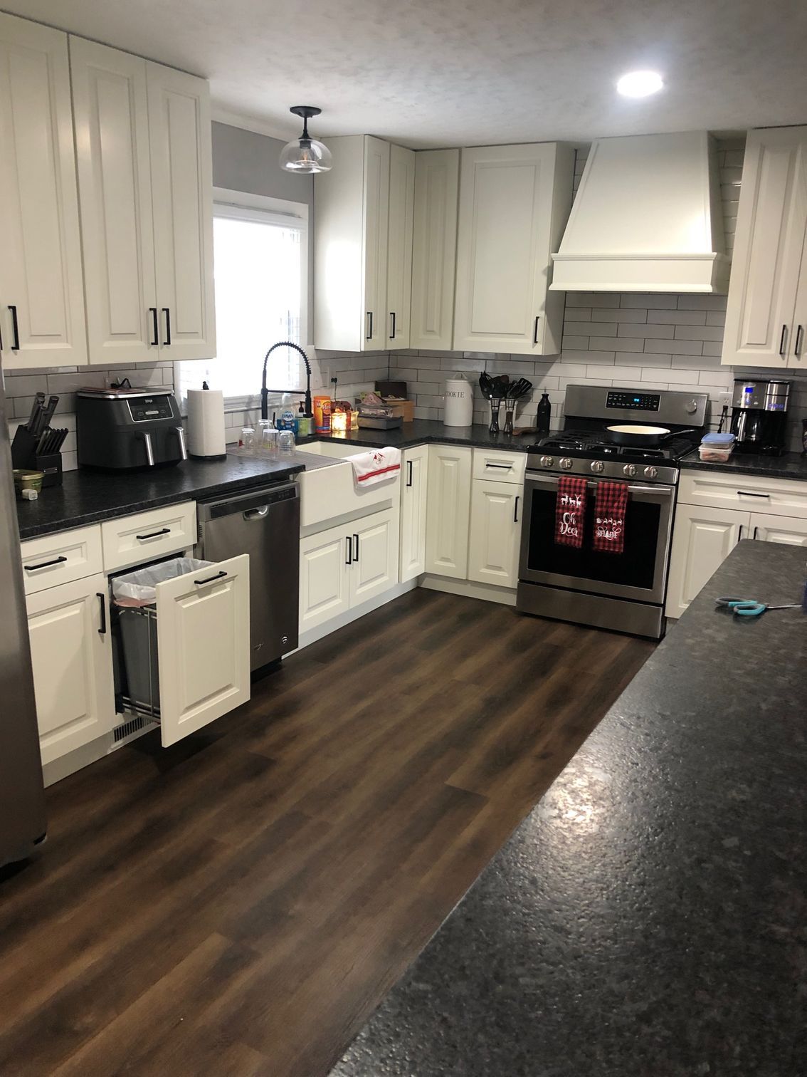 Modern kitchen with white cabinets, black countertops, dark wood floor, and stainless steel appliances