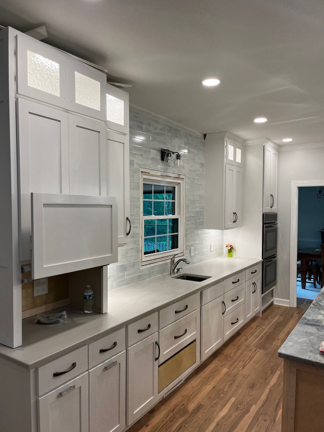 Bright white galley kitchen with gray cabinets, wood floor, and a window over the sink