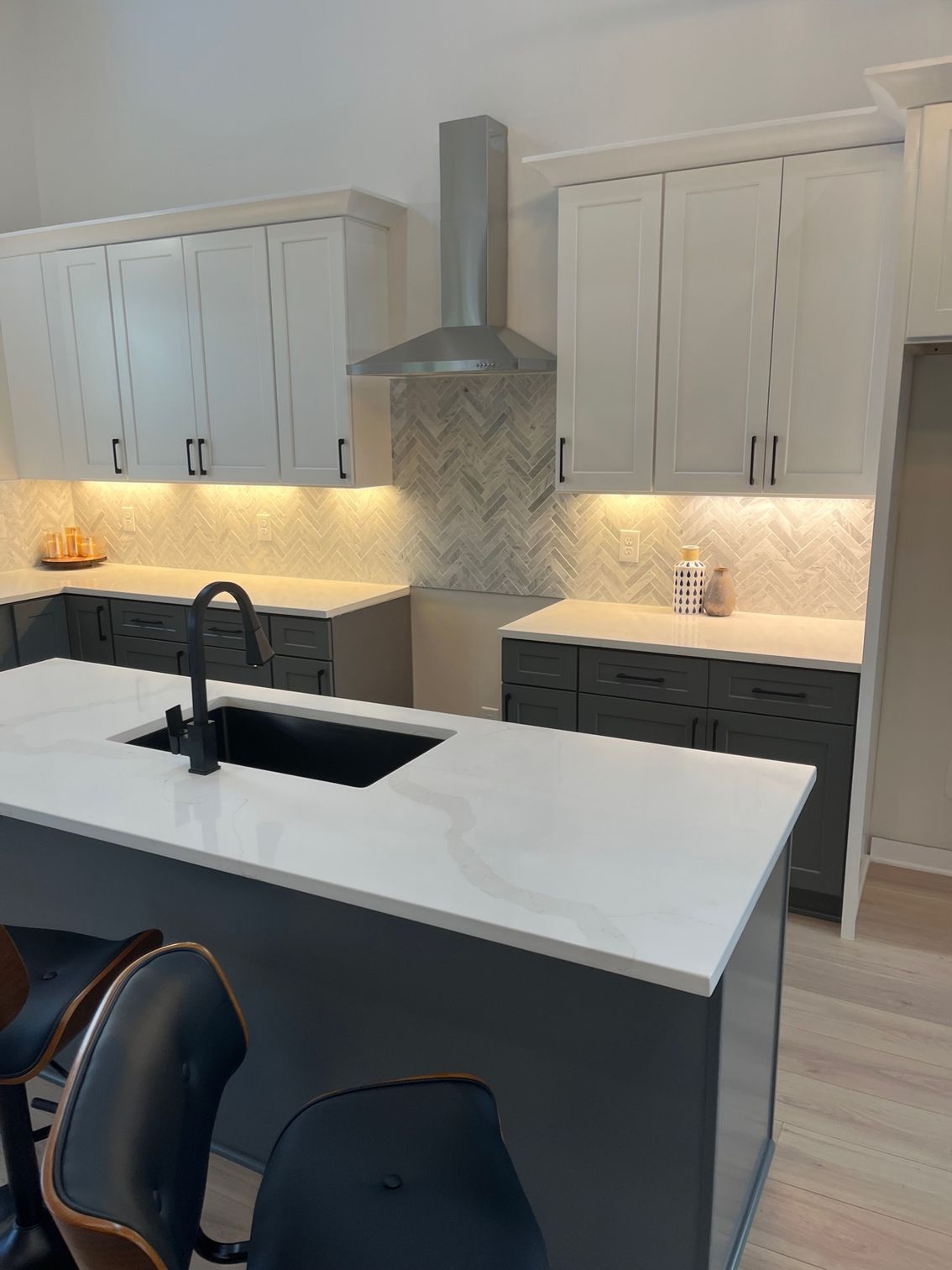 Modern white kitchen with dark island, black sink faucet, and stainless range hood