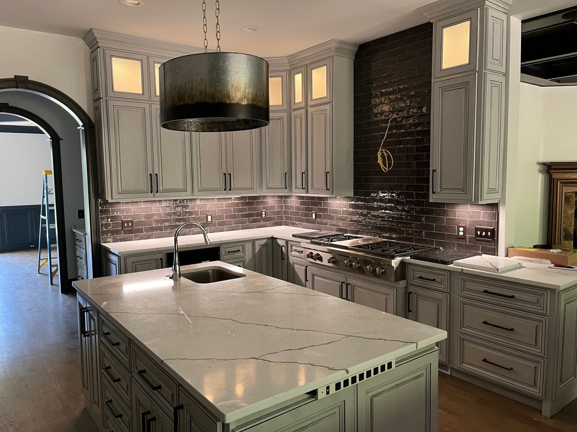 Elegant kitchen with white cabinets, a large island, dark backsplash, and pendant lighting