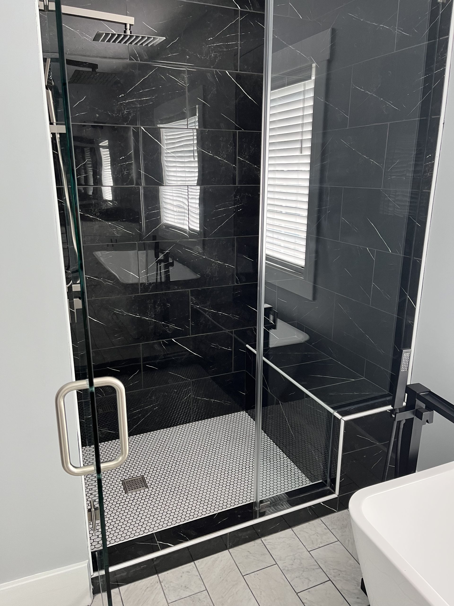 Modern black-tiled walk-in shower with glass door, white pebble floor, and a built-in bench旁