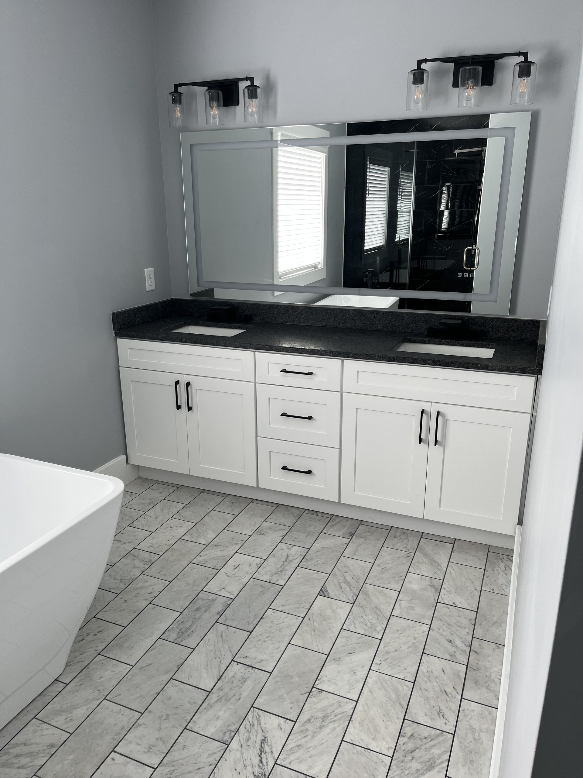 Modern bathroom vanity with double sinks, large mirror, and black countertop over white cabinets.