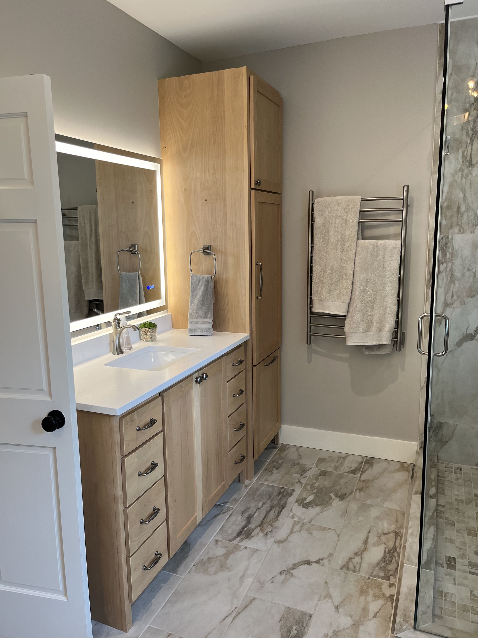 Modern bathroom vanity with wood cabinets, white countertop, mirror, towel rack, and glass shower
