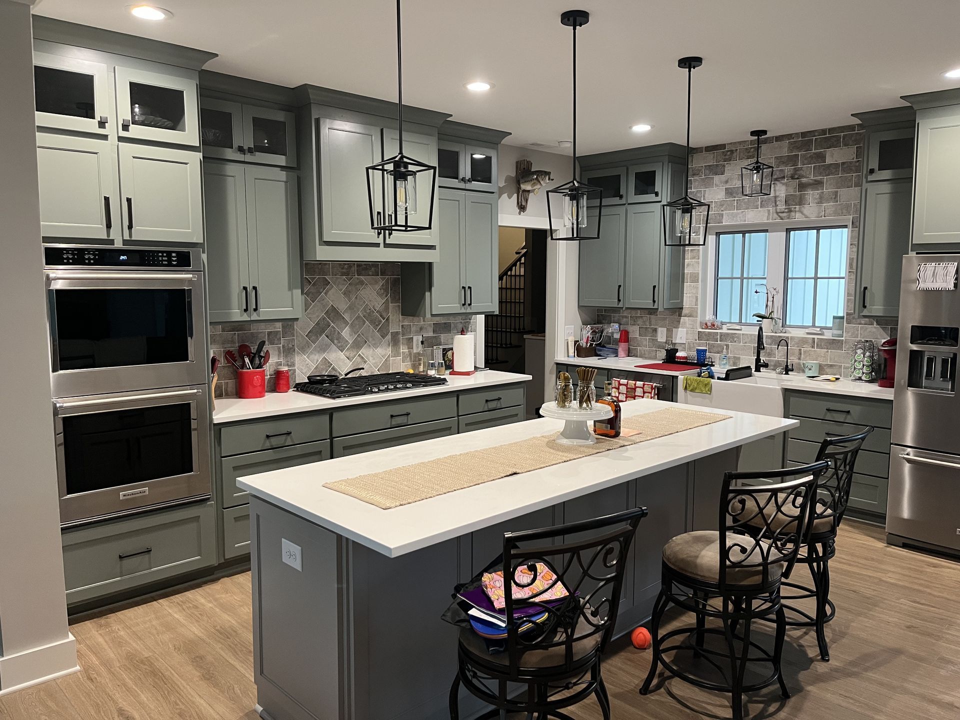 Modern kitchen with gray cabinets, large island, hanging lights, and built-in stainless steel appliances.