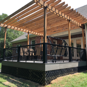 Covered wooden deck with black railing and pergola attached to a house