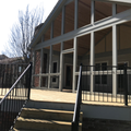 Modern building entrance with glass doors, white columns, black railings, and front steps in sunlight