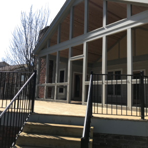 Modern building entrance with glass doors, white columns, black railings, and front steps in sunlight