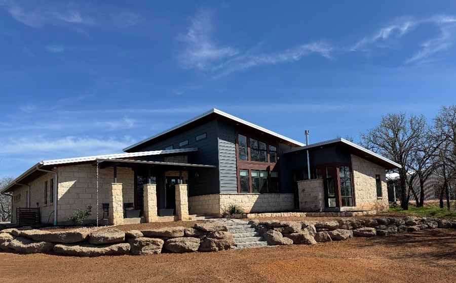 Modern home with cream stone and dark gray siding, featuring a slanted roof, large windows, and a landscaped rock terrace.