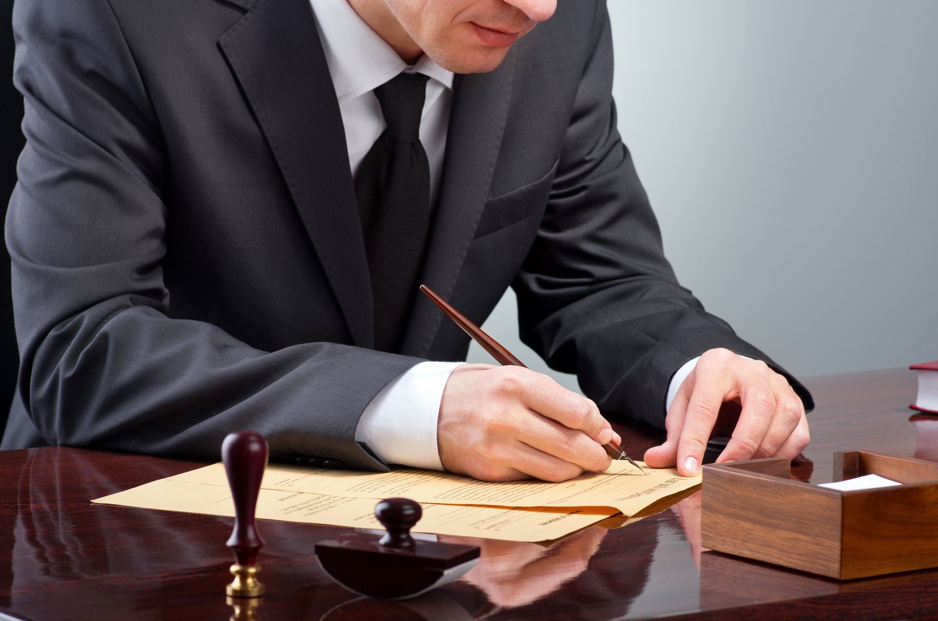 Persona in giacca e cravatta che scrive con una penna su un foglio di carta, accanto a un timbro e a un tampone.