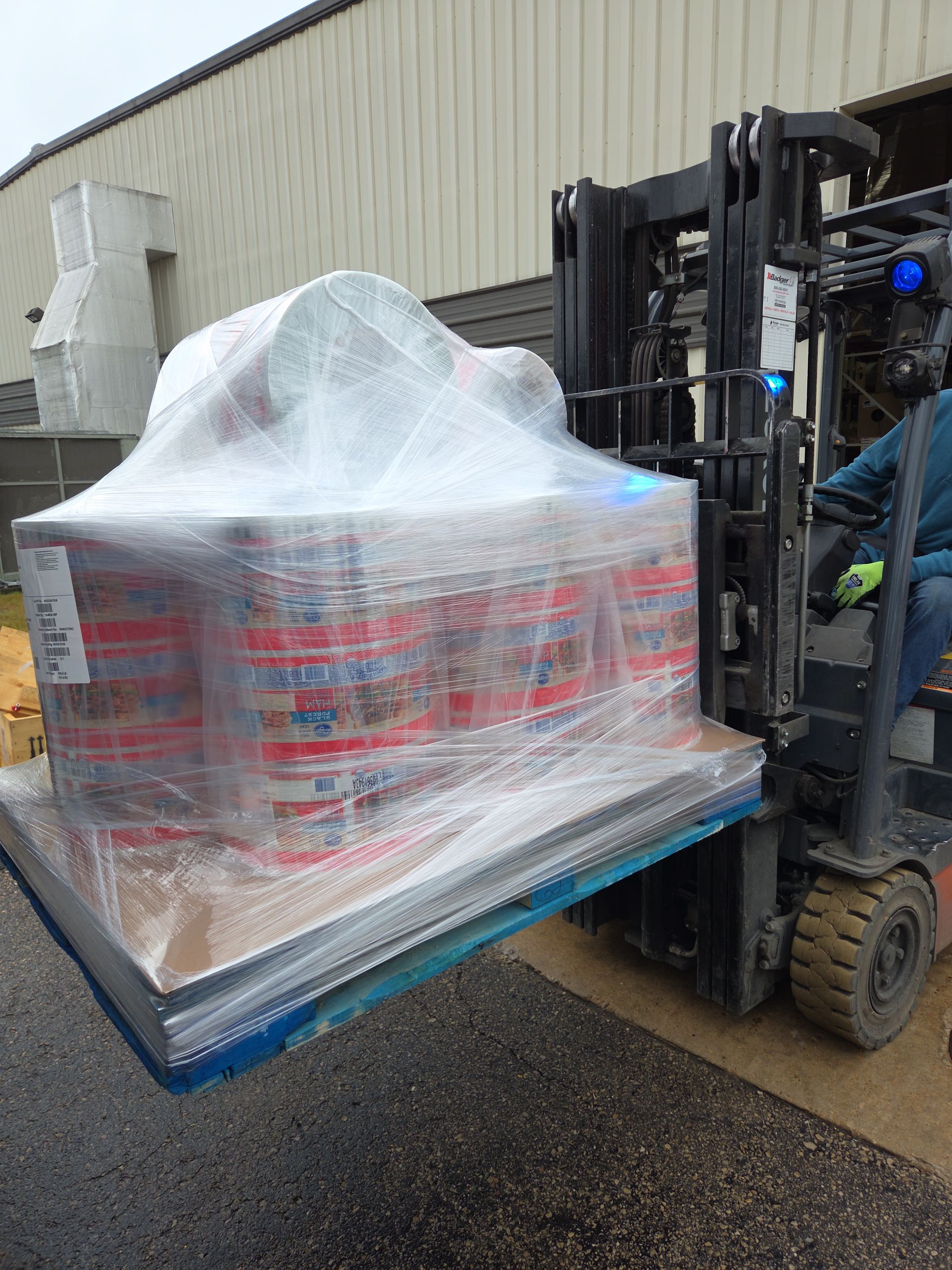 Forklift moving a shrink-wrapped pallet of large containers outside a warehouse