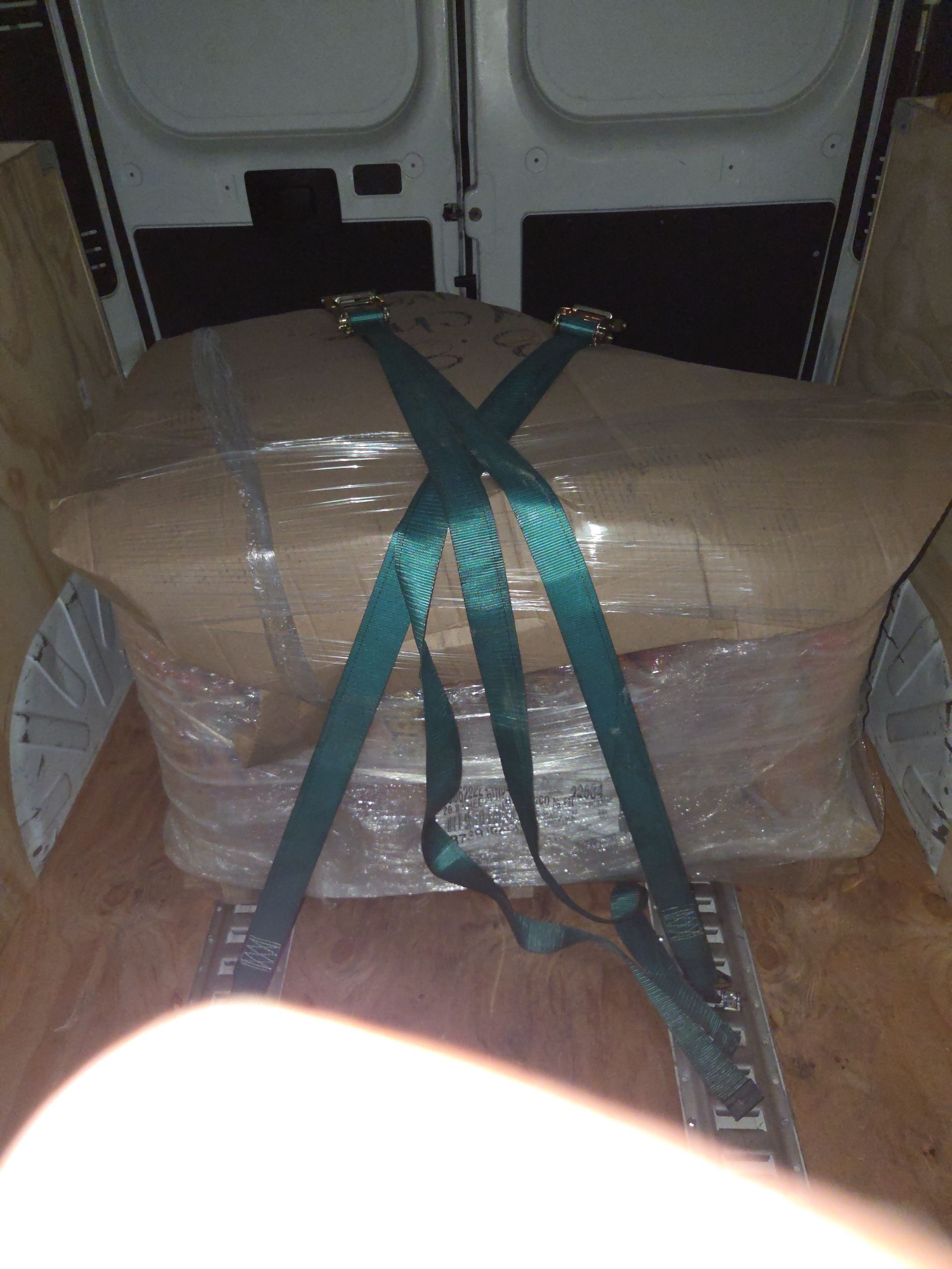 Large wrapped package secured with green straps inside a vehicle cargo area