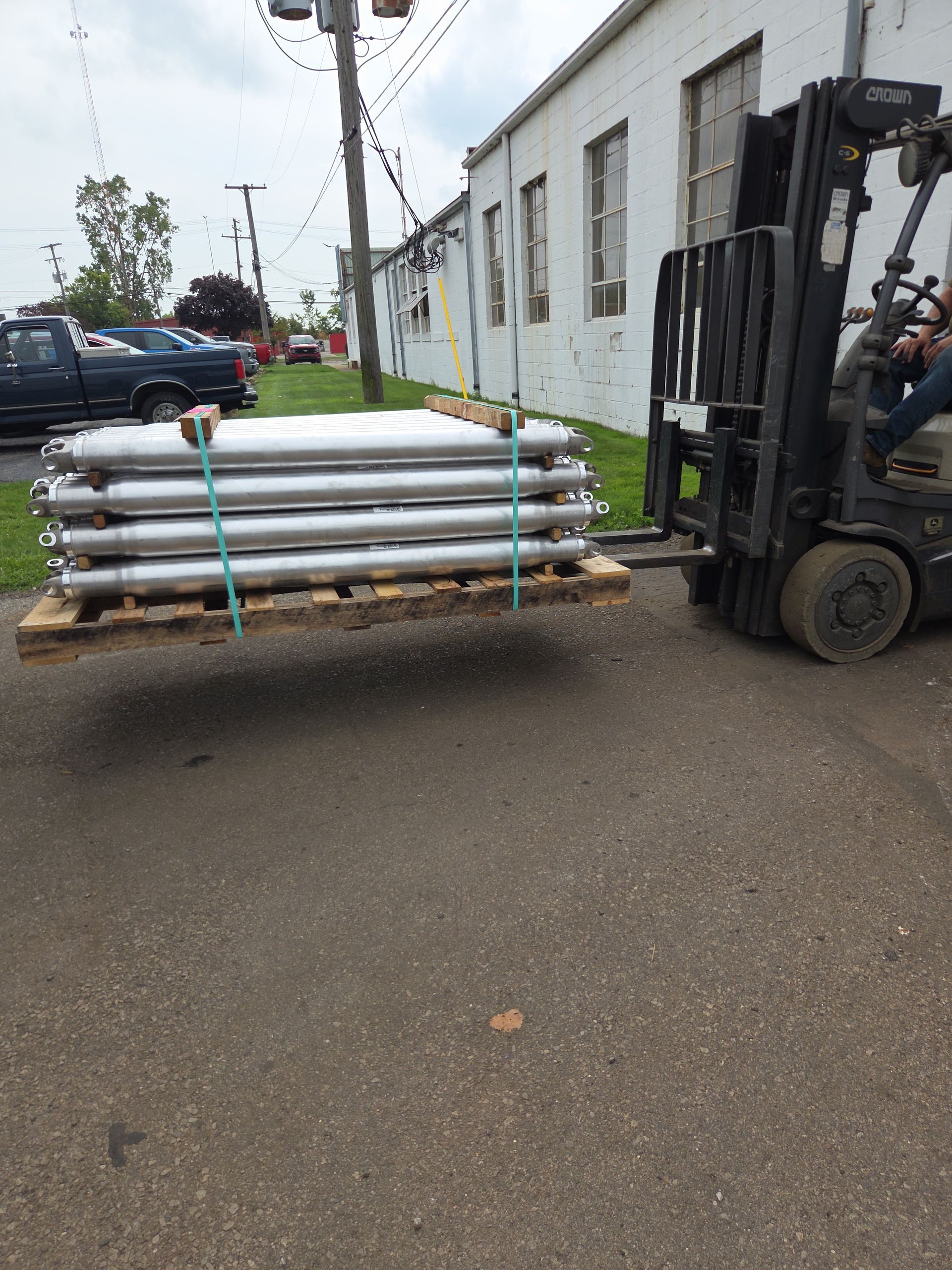 Forklift carrying stacked white pipes secured with blue straps beside a building.