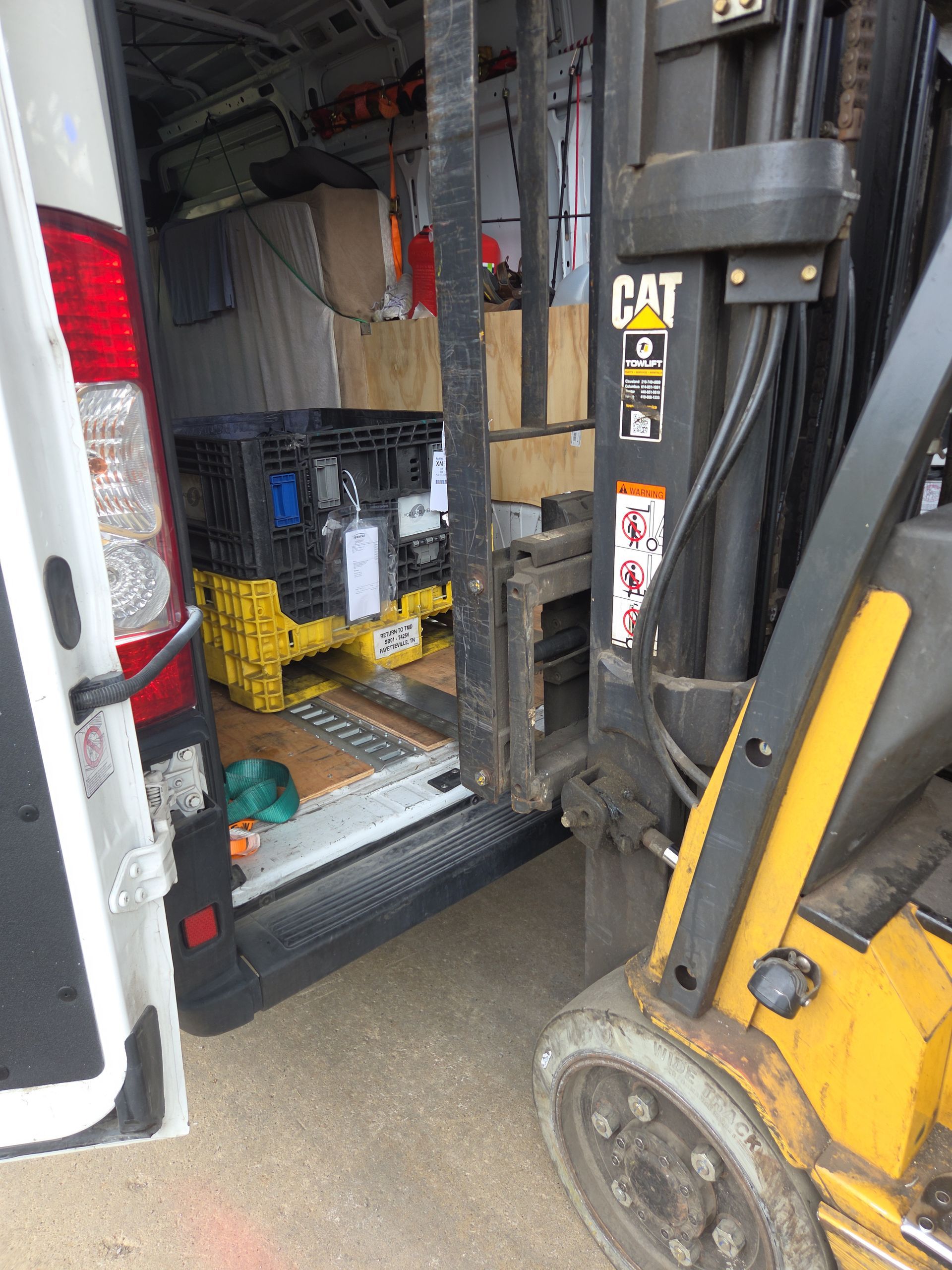 Yellow CAT forklift beside a truck loading bay with stacked crates inside