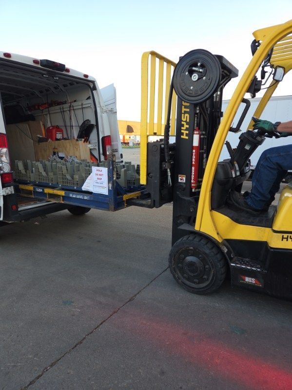 Yellow forklift loading a box into a delivery van beside a truck at a warehouse dock