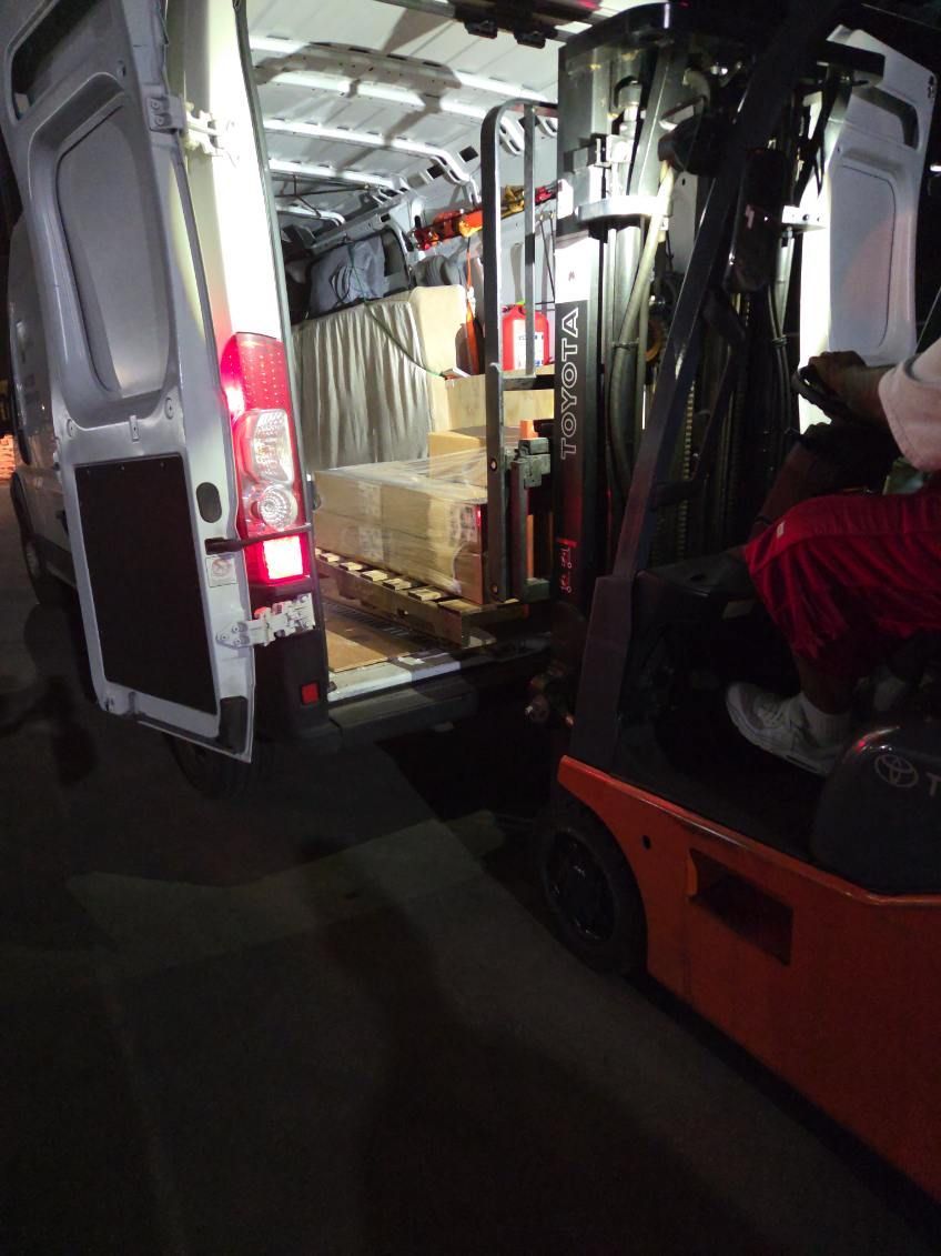 Loading van interior with stacked boxes and an orange forklift lifting cargo.