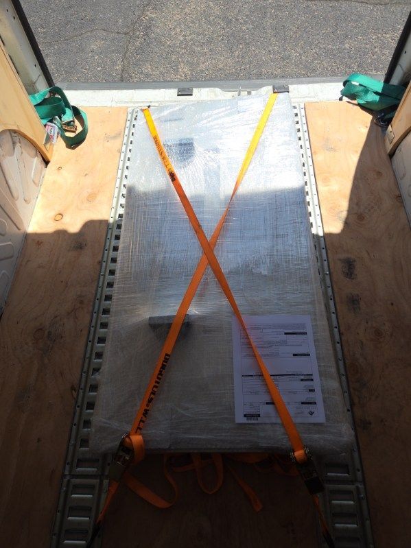 Orange straps securing a metal crate or panel inside a truck or trailer