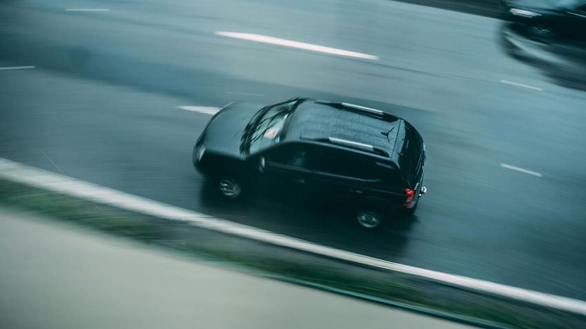 Black SUV driving on a blurred wet road, seen from above.