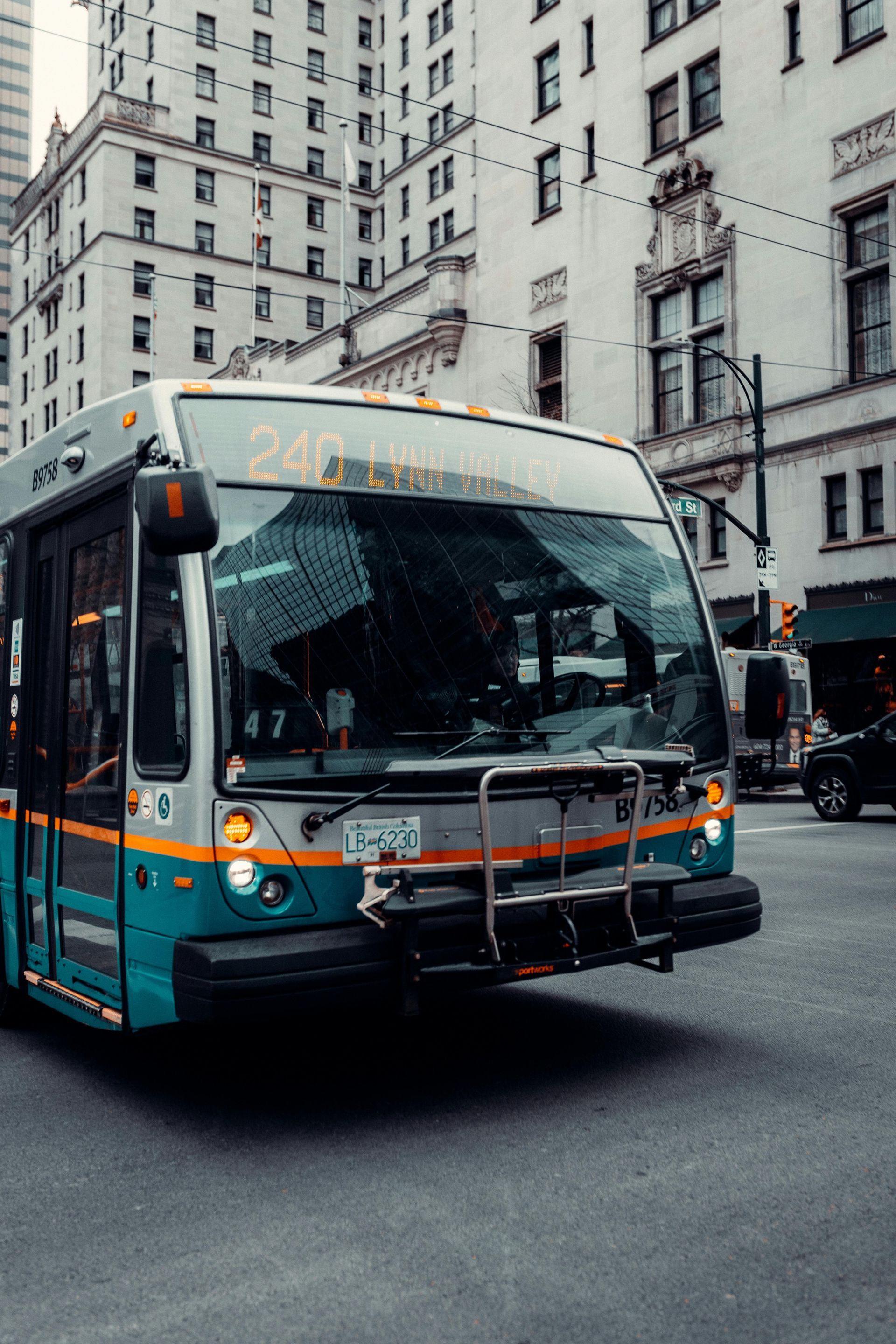 Teal city bus turning at an intersection beside tall urban buildings.
