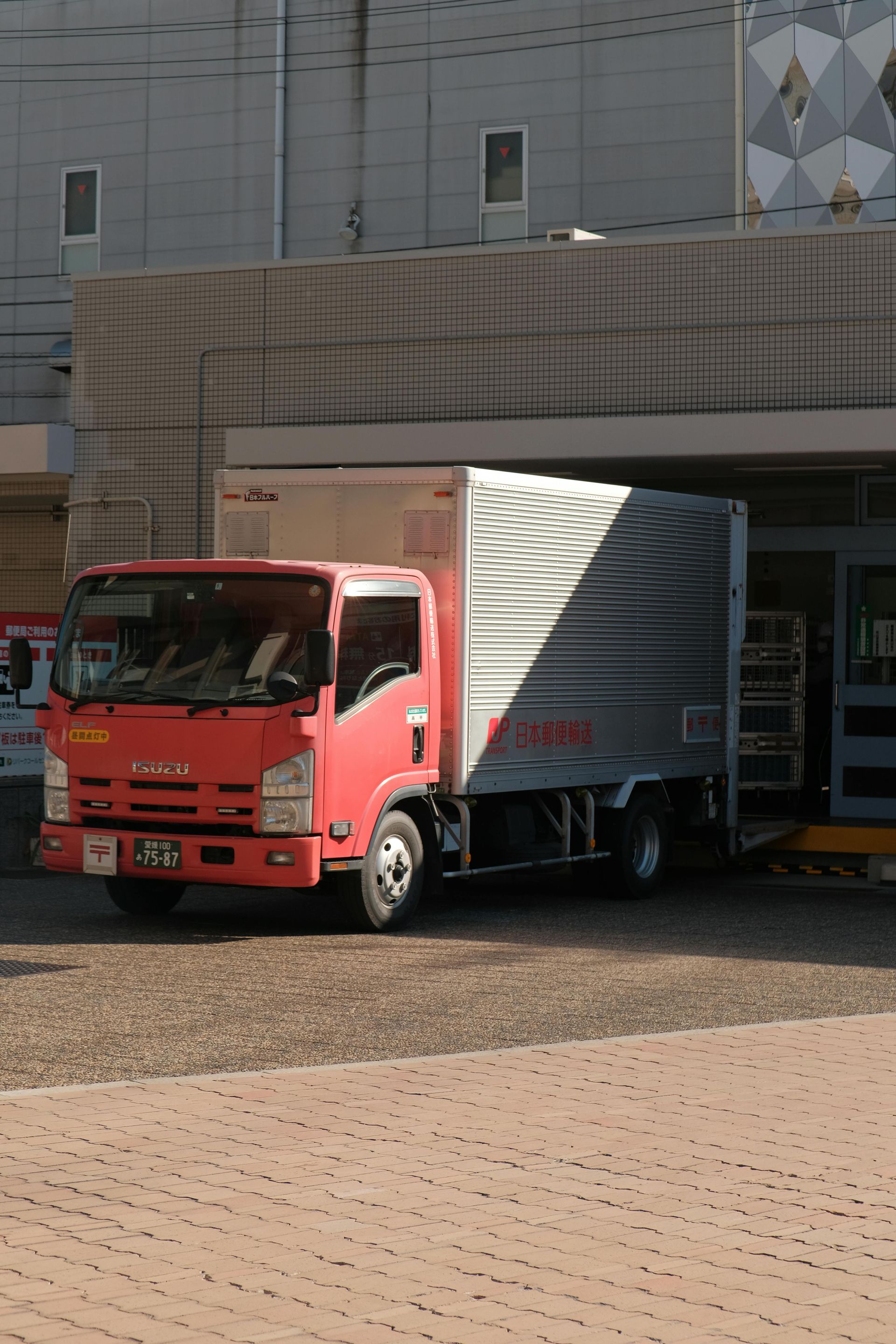 Red delivery truck parked under a building entrance on a cobblestone street.