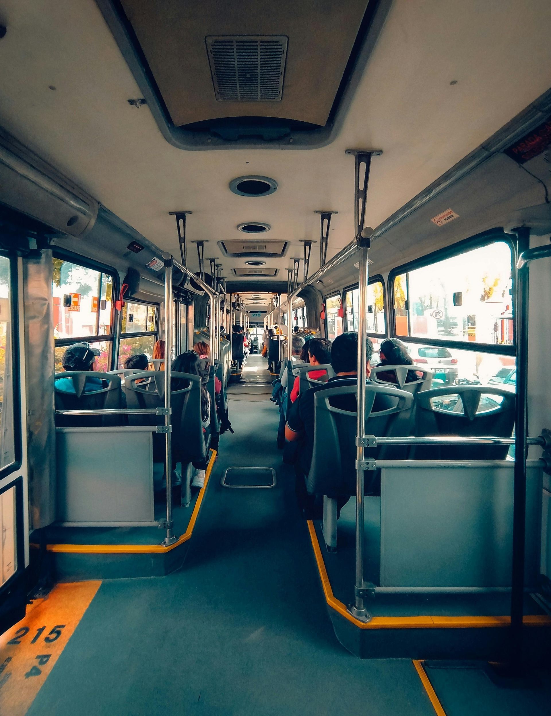 Interior of a city bus with rows of seats and passengers, viewed down the aisle toward the front.
