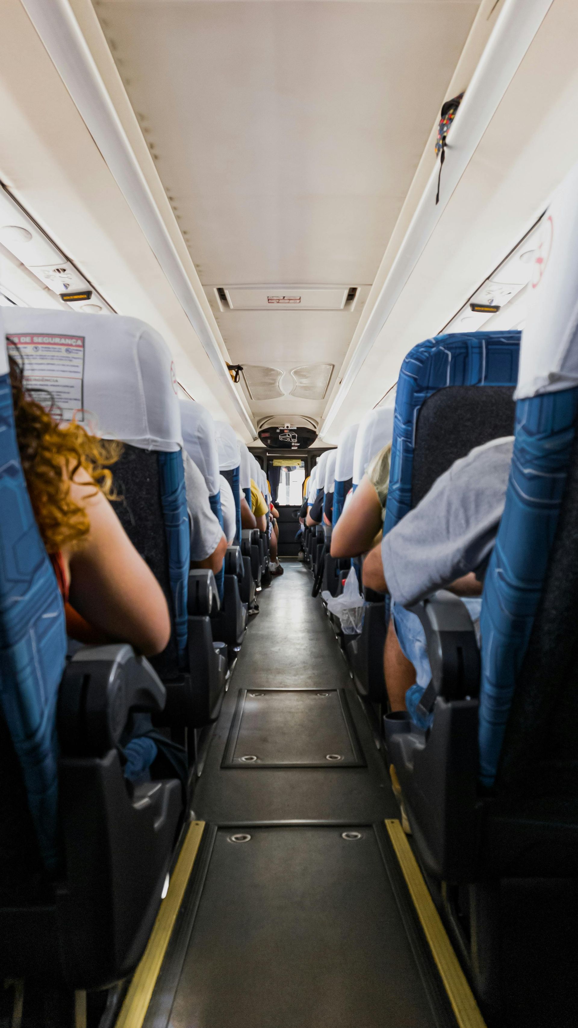 Passengers seated inside a narrow train carriage, viewed down the aisle toward the front.