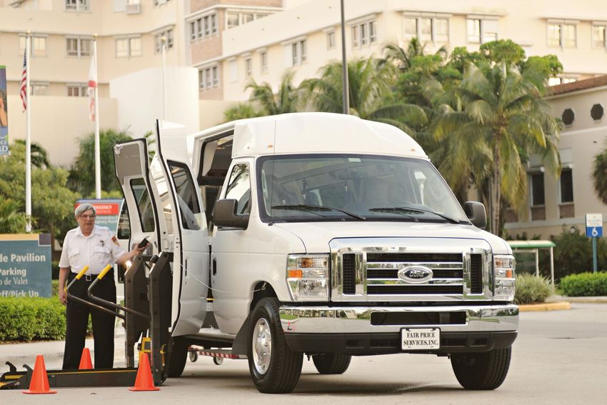 White delivery van with open doors beside a worker and traffic cones on a street