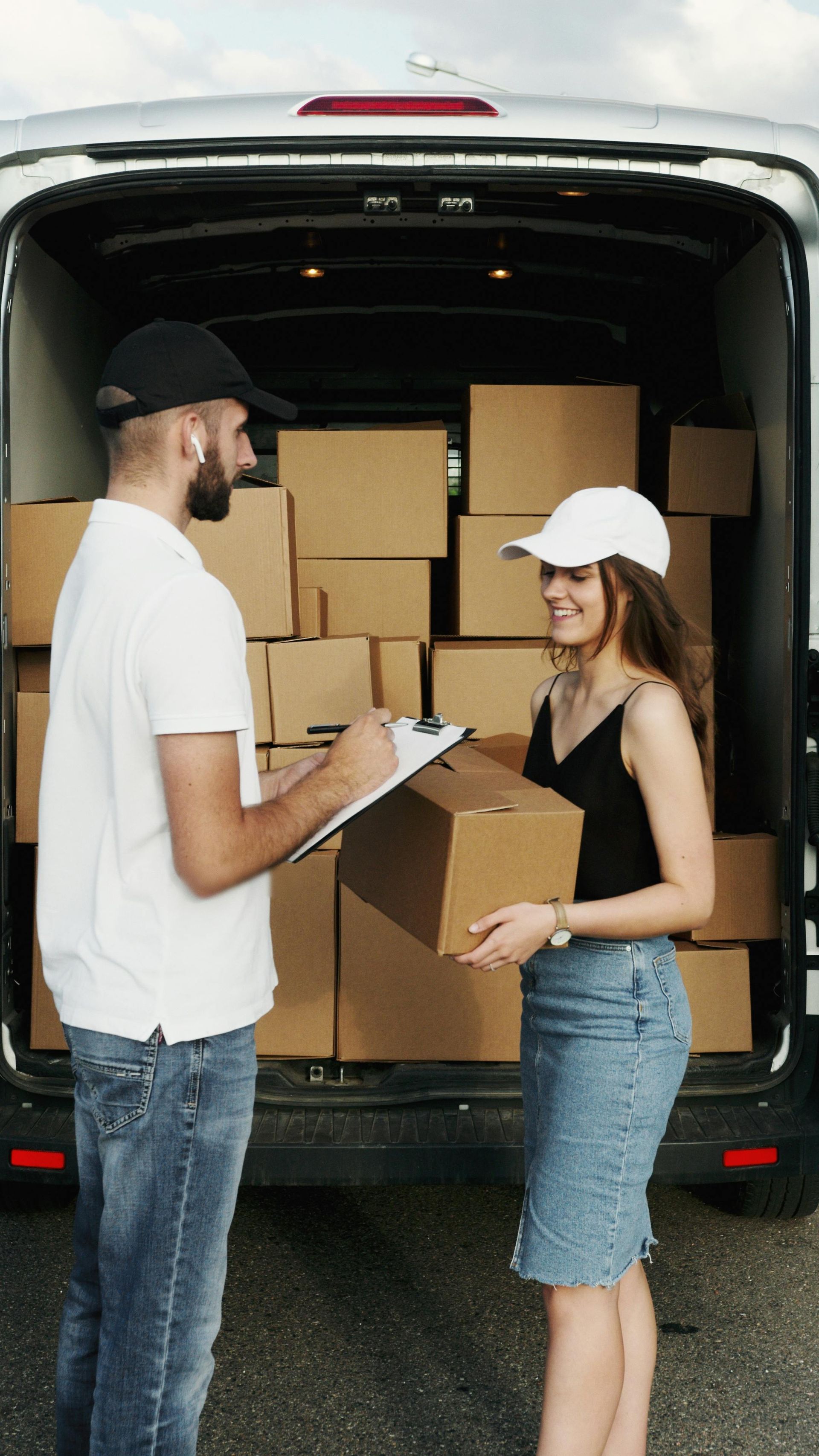 Two movers load cardboard boxes into a delivery van while checking a clipboard.