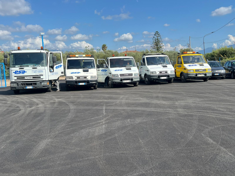 Cinque carri attrezzi bianchi parcheggiati in un parcheggio sotto un cielo azzurro.