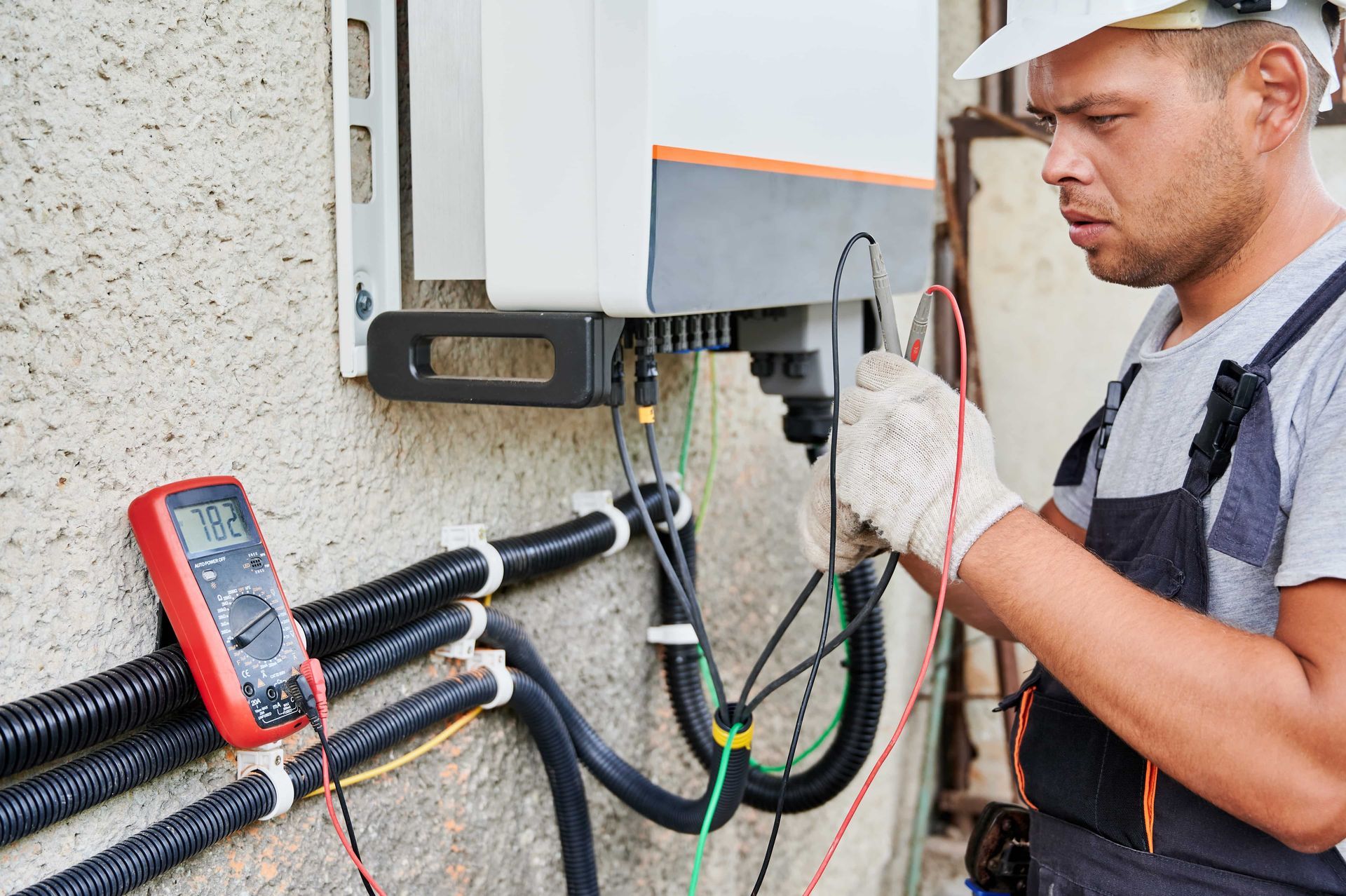 Electrician testing outdoor electrical box with a multimeter and wires