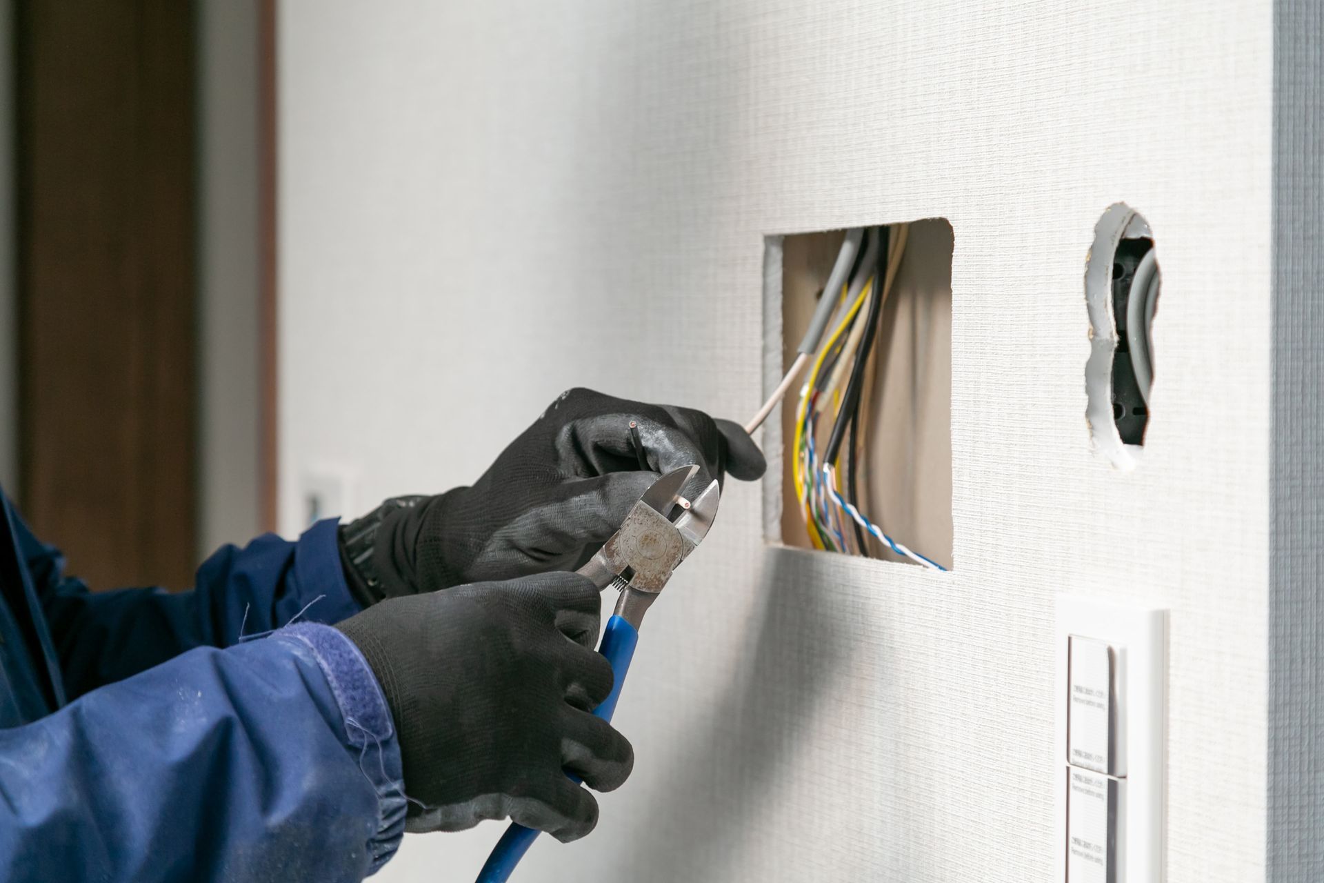 Gloved electrician repairing exposed wiring in a wall opening with pliers