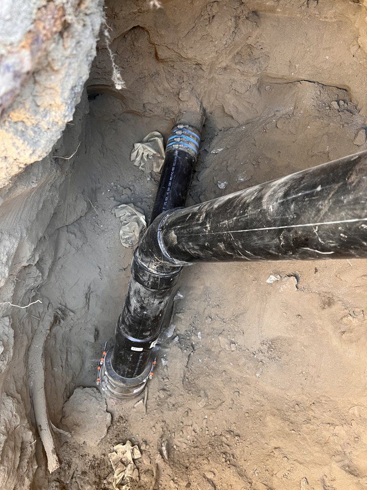 A black pipe is sitting in the dirt next to a rock.