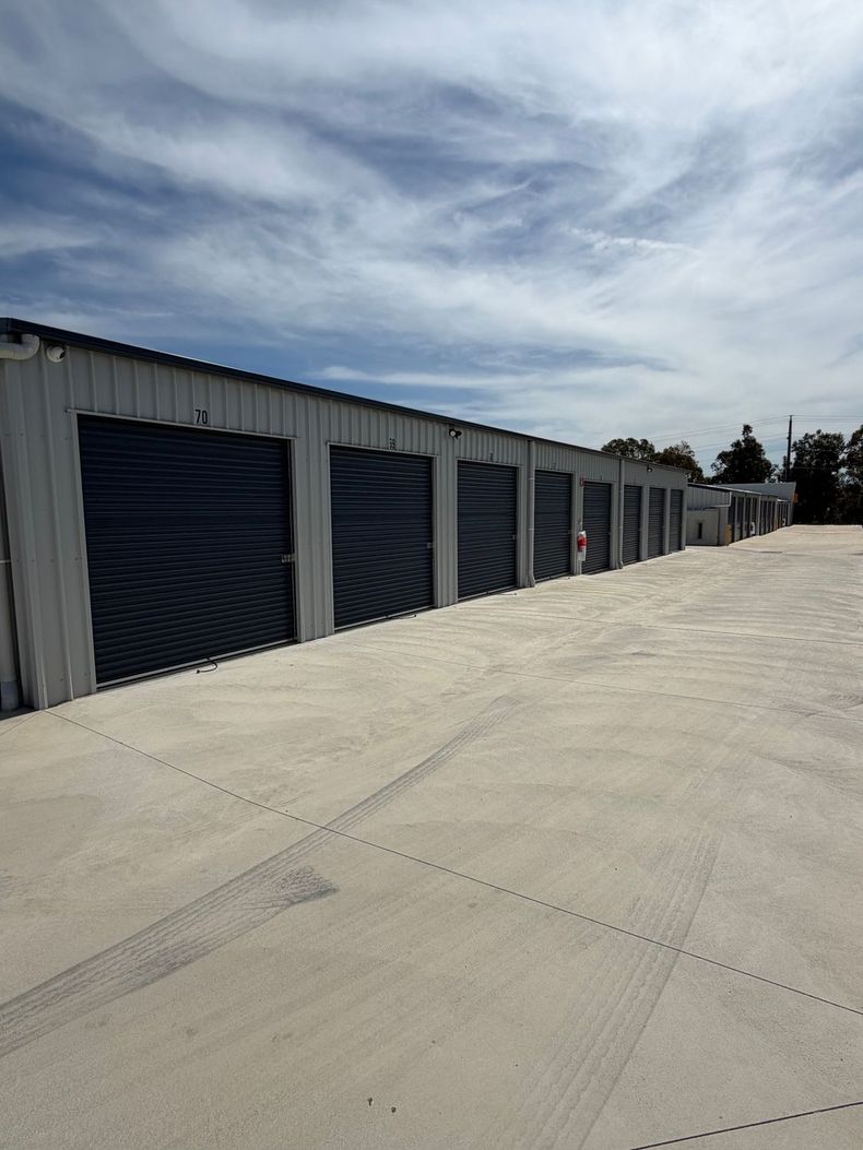 Row of white storage unit garages along a paved lane on a sunny day