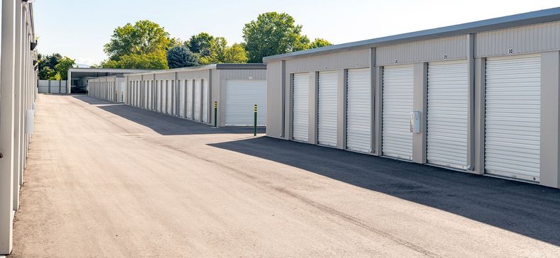 Row of white storage unit garages along a paved lane on a sunny day