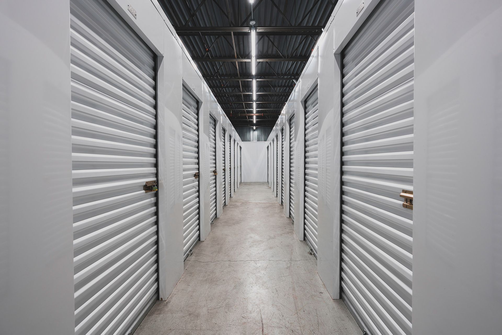 Long storage hallway with closed white roll-up doors on both sides, lit by overhead lights.