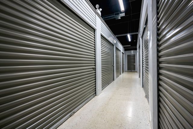 Empty storage corridor with closed metal roll-up doors and bright overhead lights