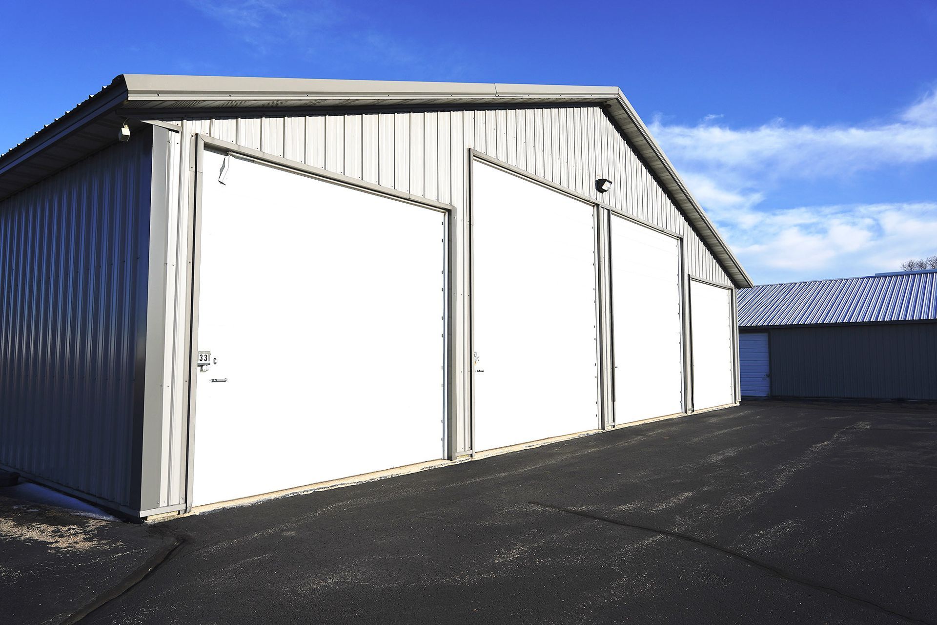 White storage building with large garage doors on a paved lot under a blue sky