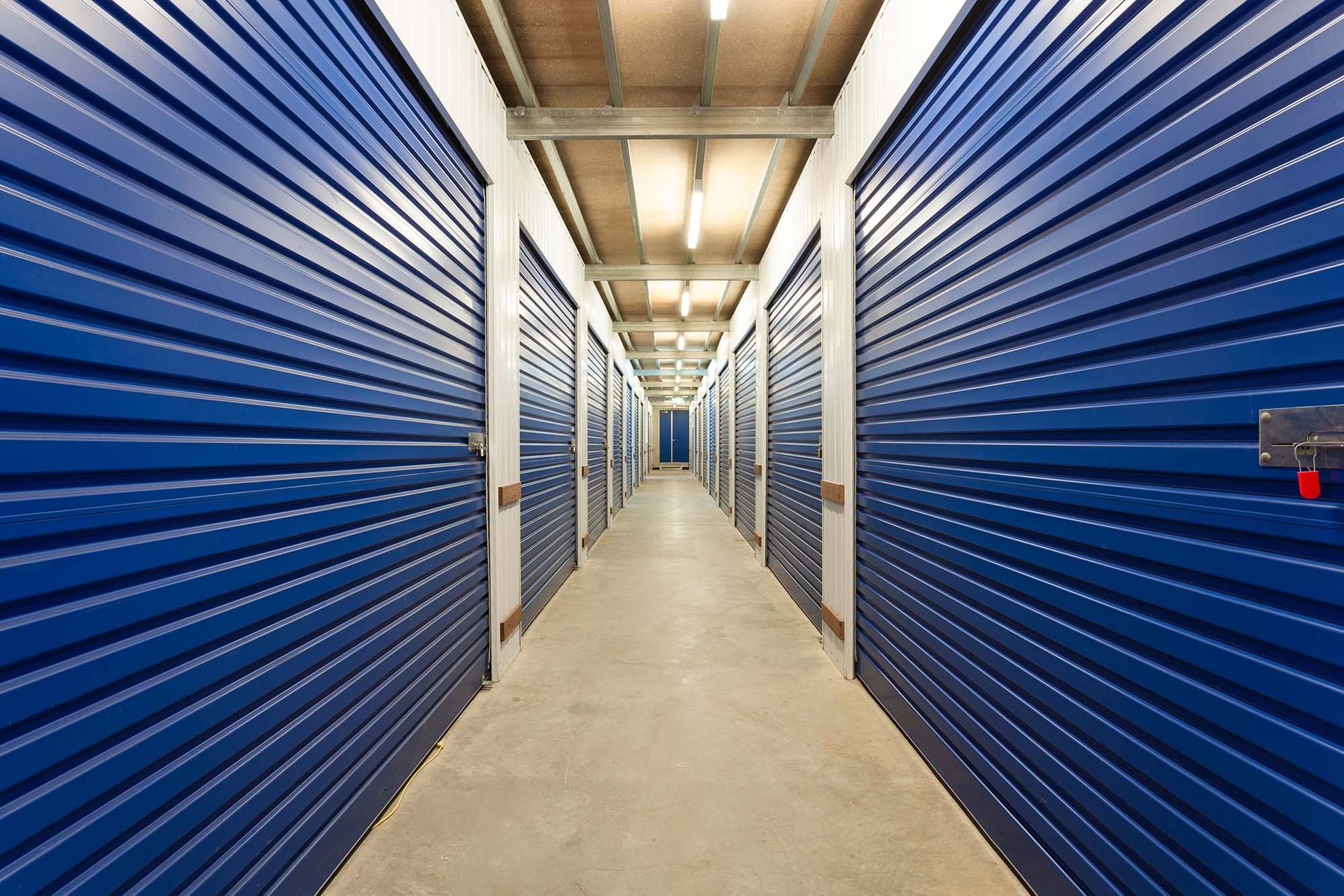 Long hallway with blue storage unit doors on both sides and a concrete floor
