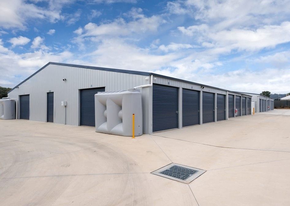 Row of white storage unit doors along a beige building beside a gravel lot under a blue sky